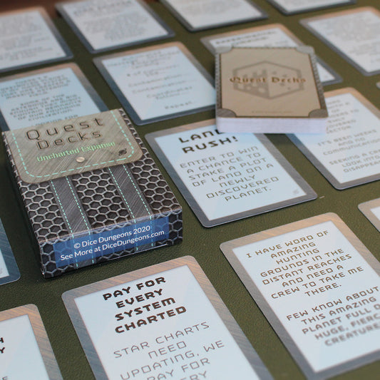 Uncharted Expanse Quest Deck laid on a table surrounded by small stacks of cards from the deck in a uniform grid across the table, except one deck which has been laid across the others at an angle. The bottom of the quest deck box is in focus, which days "Dice Dungeons 2020 See More at DiceDungeons.com"