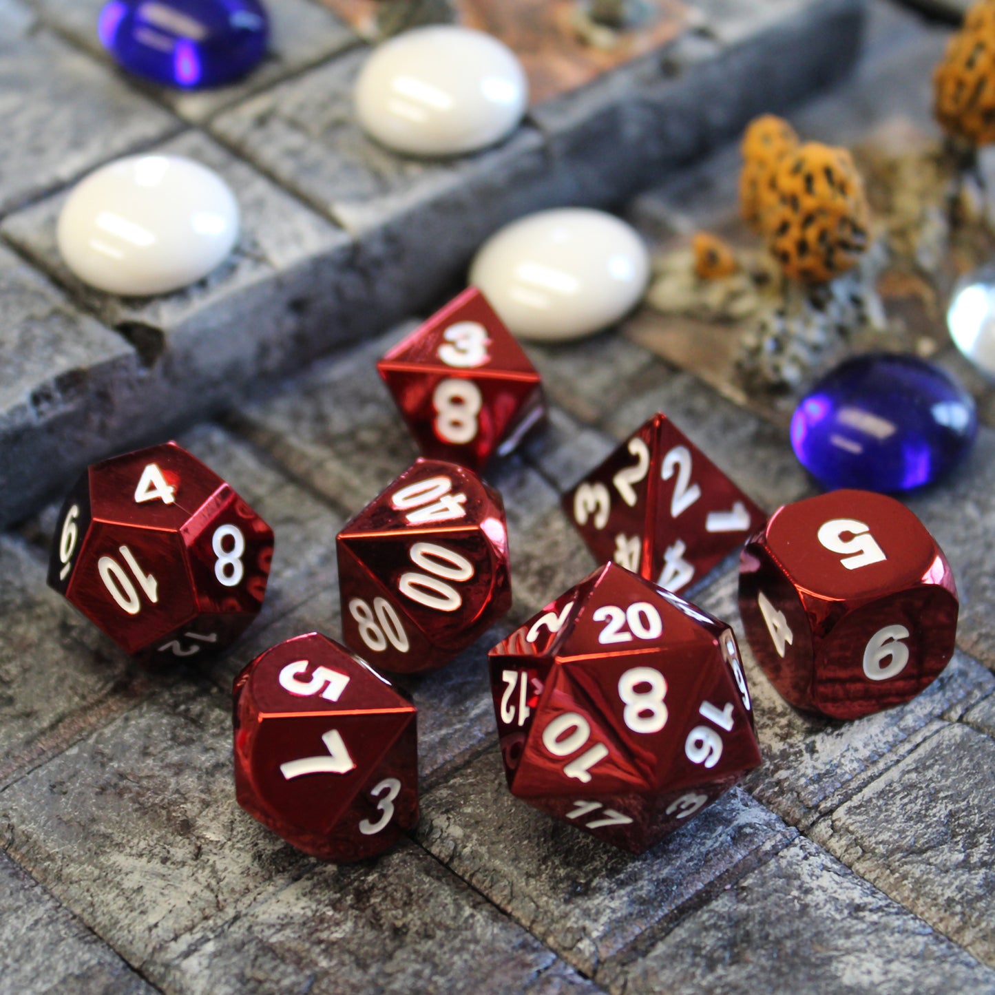 Radiant red dice set scattered on a stone floor set piece, with purple and white cabochons and other set pieces behind them