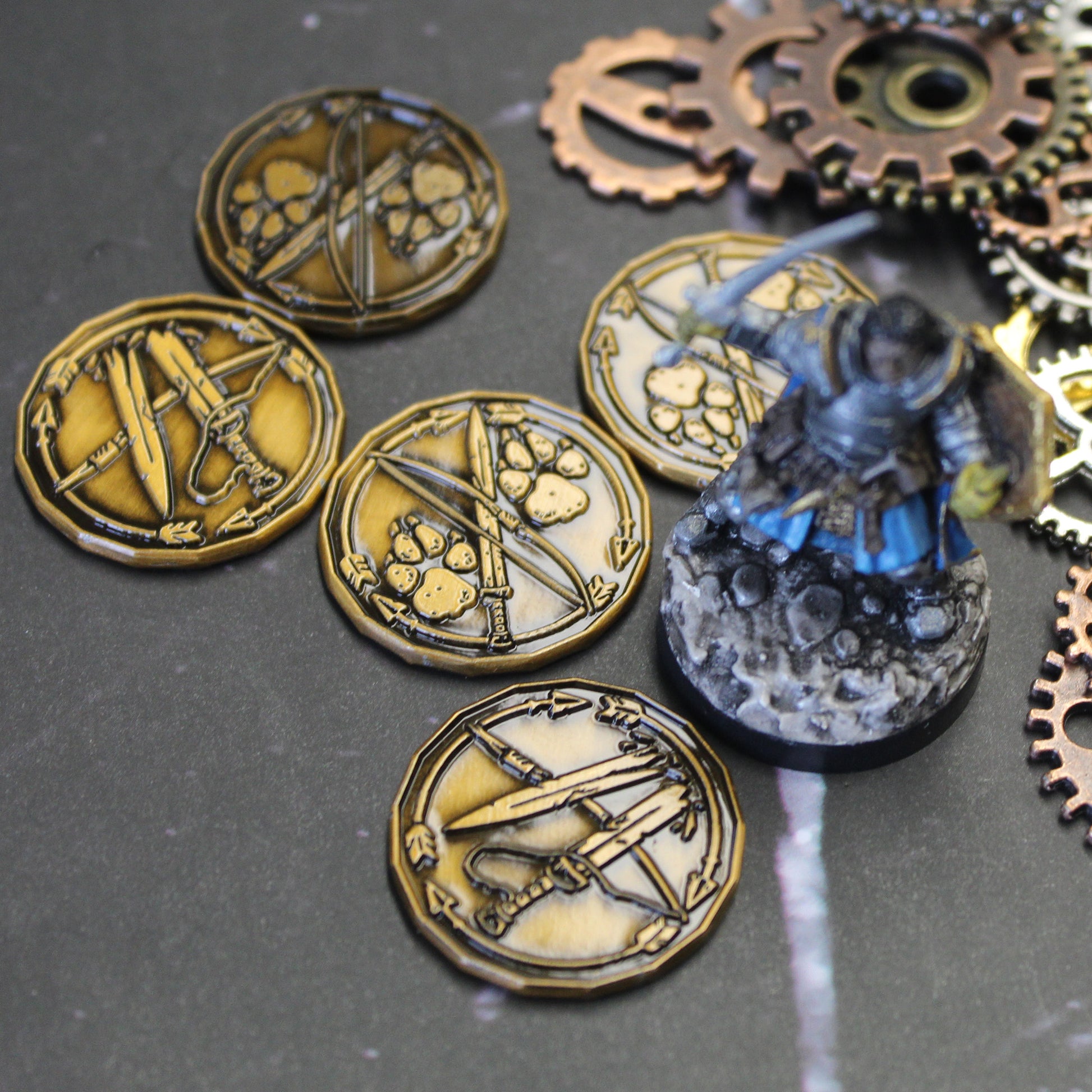 A few golden ranger character tokens sitting on a black mat next to some scattered metal gears and a miniature figure of a warrior