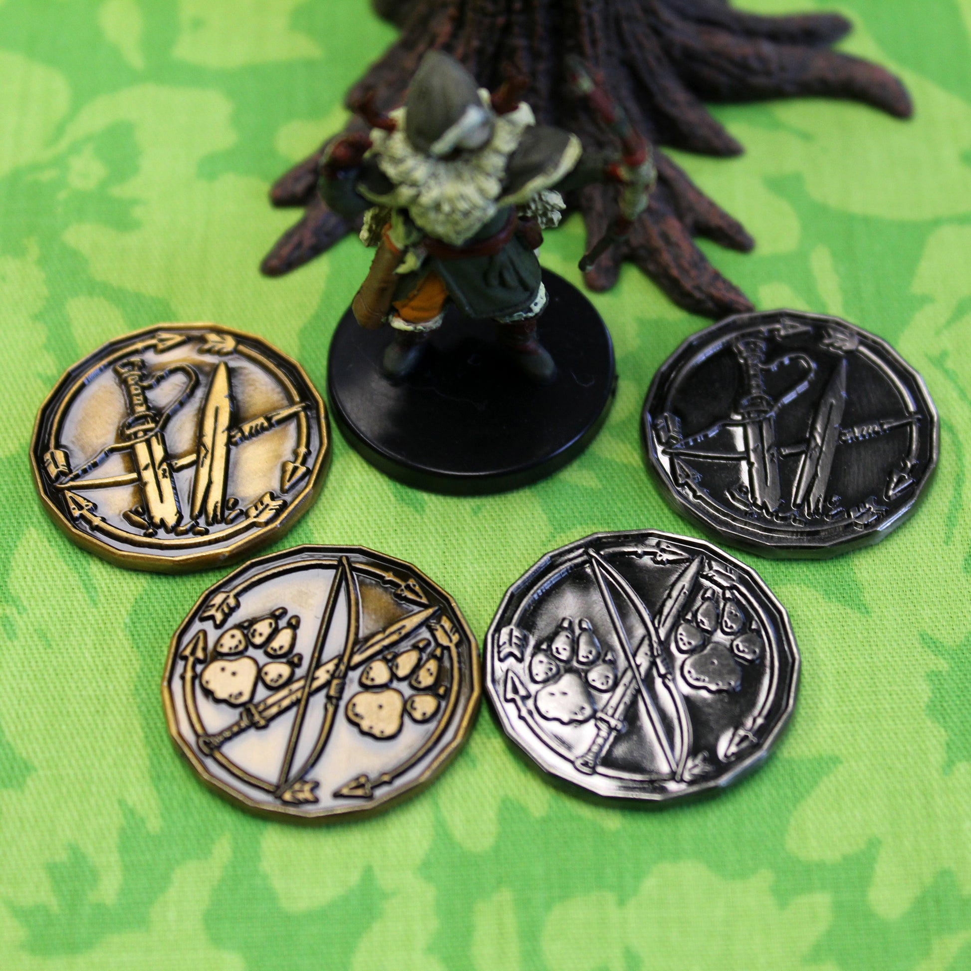 Four ranger character tokens, two silver and two gold, sitting on a green play mat next to a miniature figure
