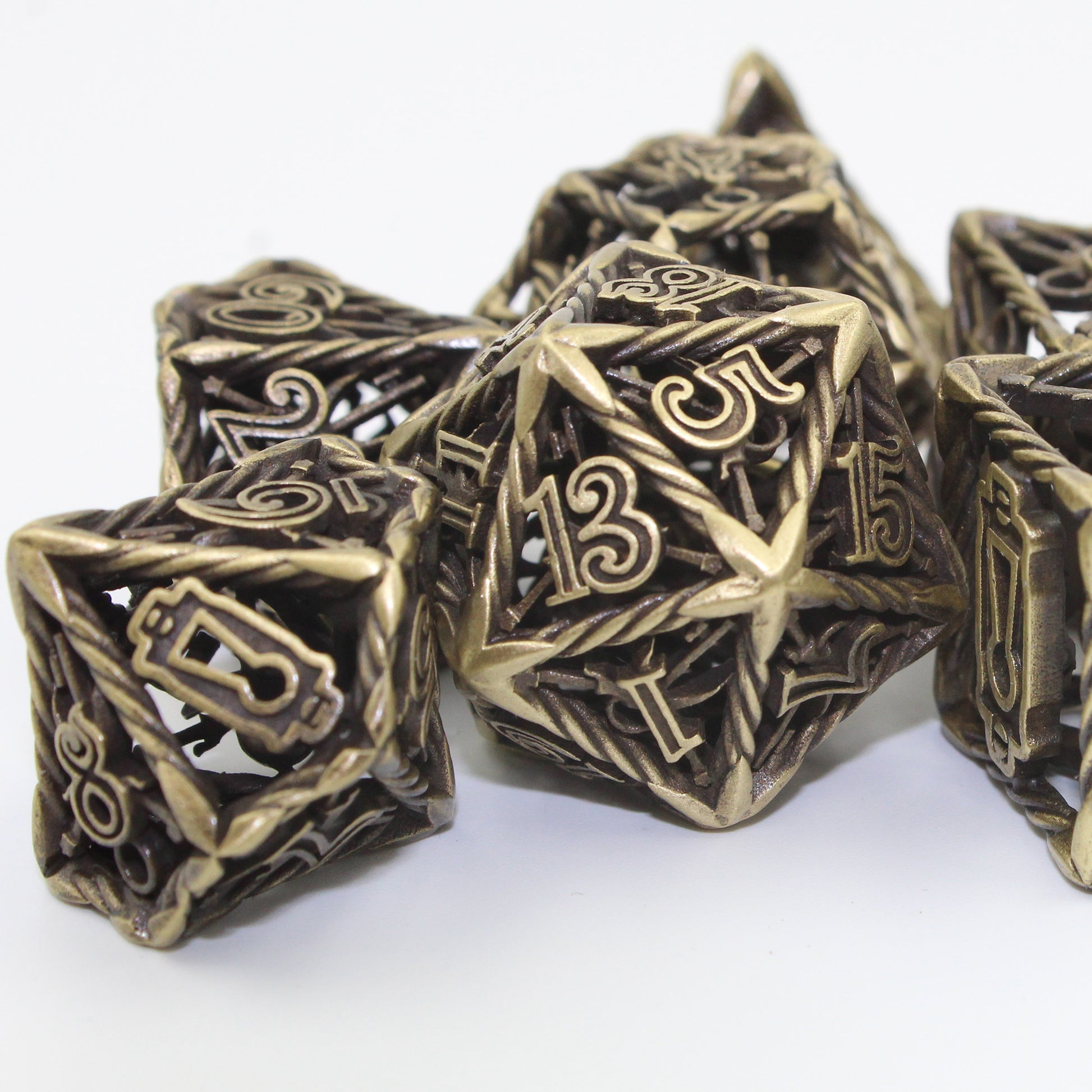 Close up of bronze Rogue die set, arranged in a pile on a white background and surface. The D20 die is in focus in the center, with the 13 and 5 sides clearly visible.