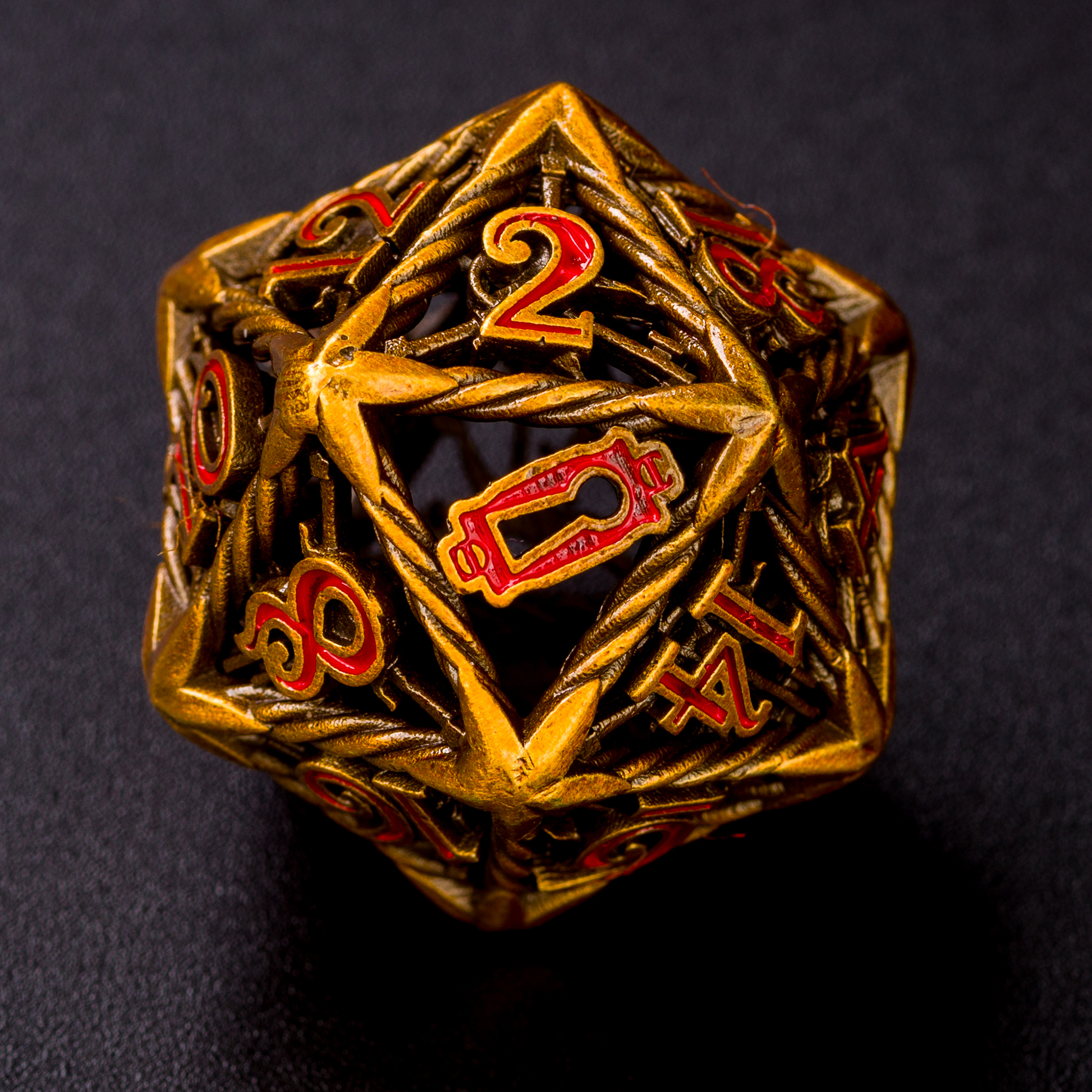 Up close gold Rogue D20 die on a black surface. The die is turned to the 20 side, showcasing the replacement of the 20 with a keyhole. The keyhole and all other numbers are inked with red.