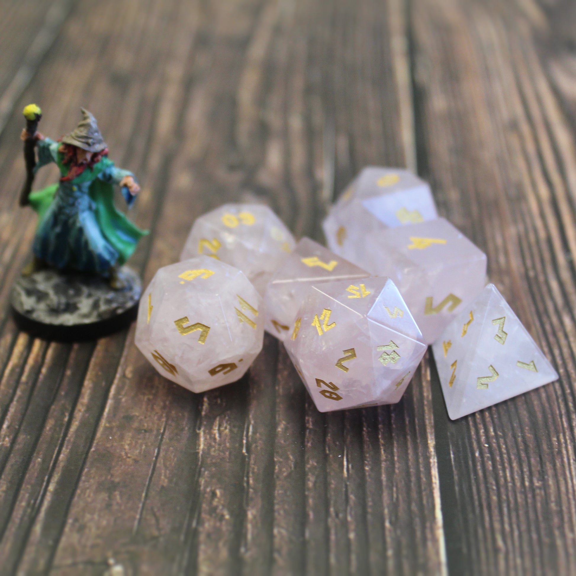 Rose Quartz dice set placed next to a miniature, featuring the soft pink gemstone and gold numbers, perfect for D&D or other roleplaying games. (mini not included)