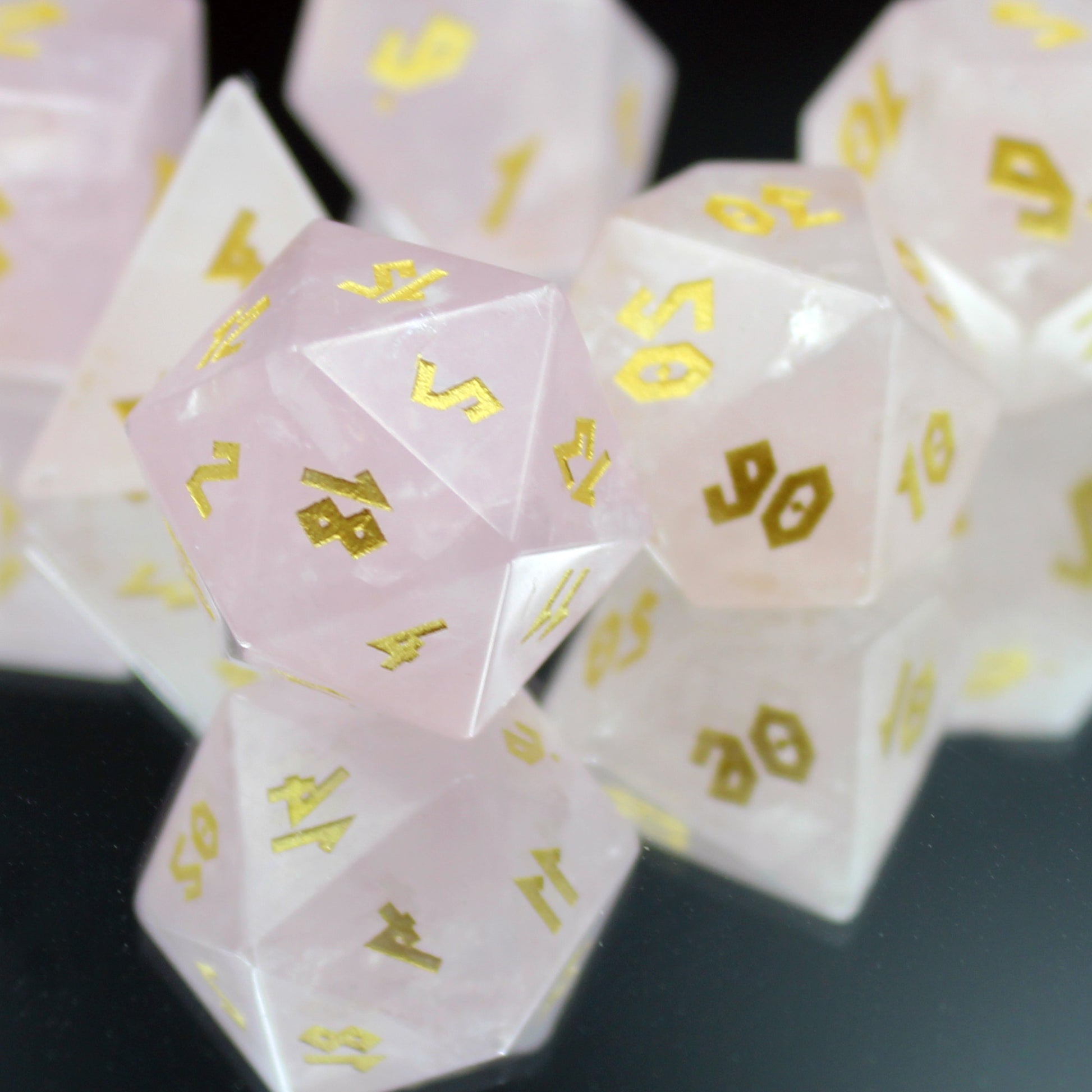 Rose Quartz dice set displayed on a mirror, highlighting the translucent pink gemstone and gold inking, ideal for 5e or TTRPG adventures.