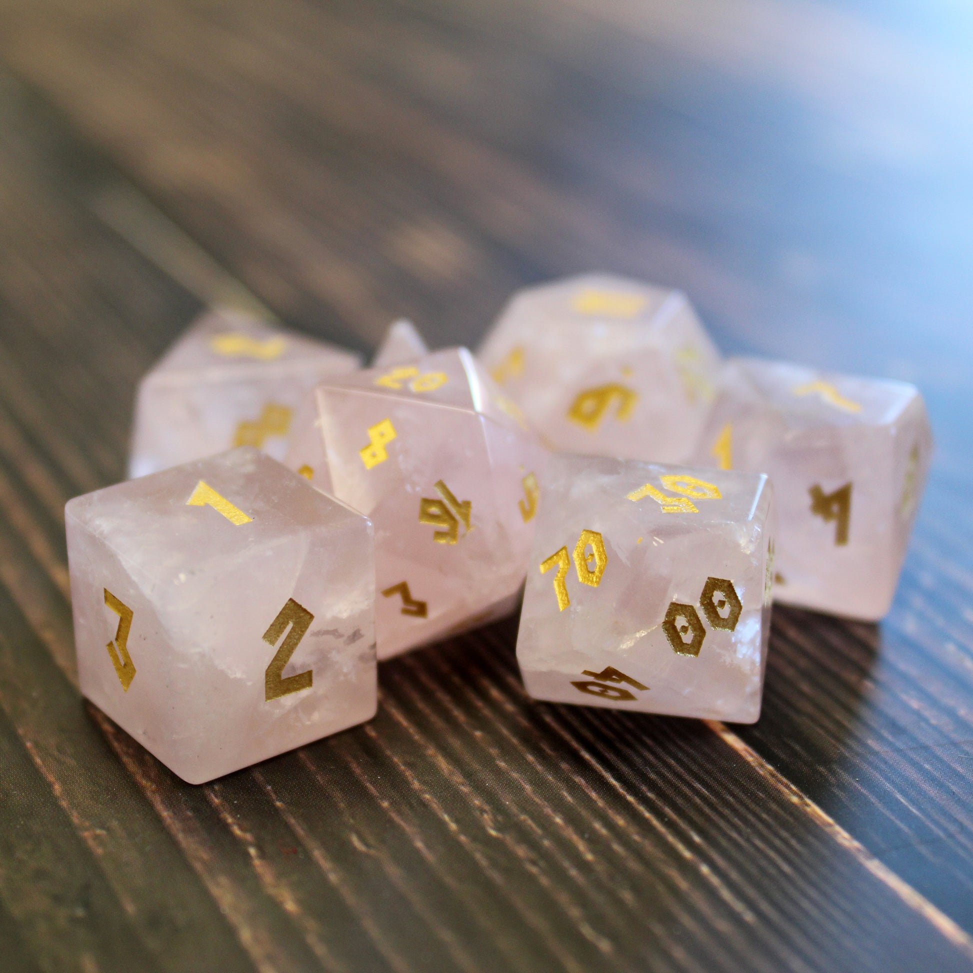 Rose Quartz gemstone dice set grouped on a table, with soft pink tones and gold numbering, perfect for Dungeons & Dragons or other RPGs.