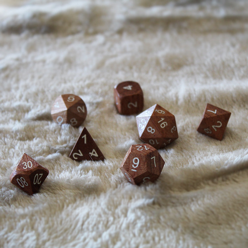 Rose Wood tabletop role playing game dice on a white fur surface. The d12 is center showing the standard underline notation for distinguishing similar numerals.