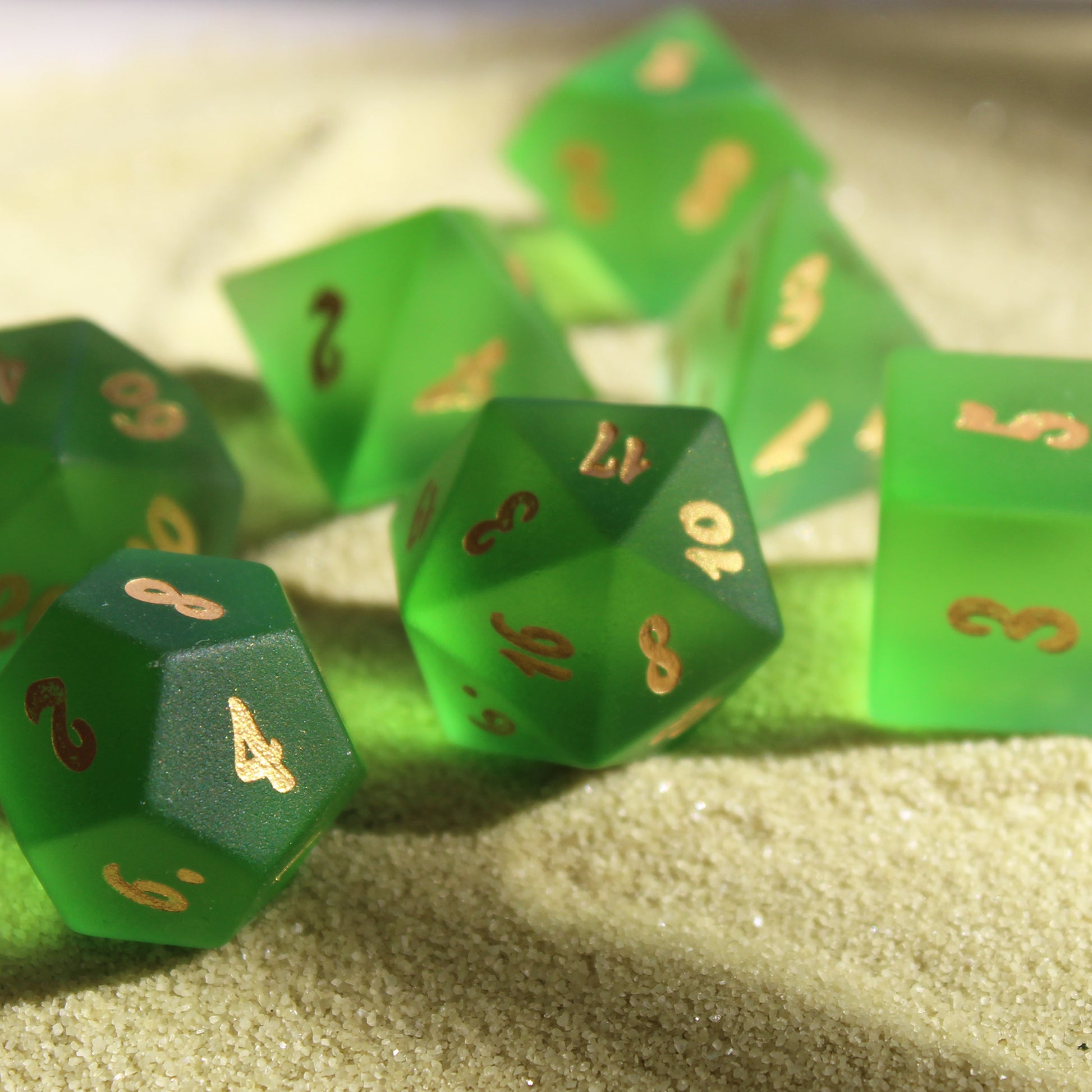 Sea Glass dice set displayed on sand in natural light, featuring frosted glass with ocean-themed numbers, perfect for Dungeons & Dragons and other RPGs.