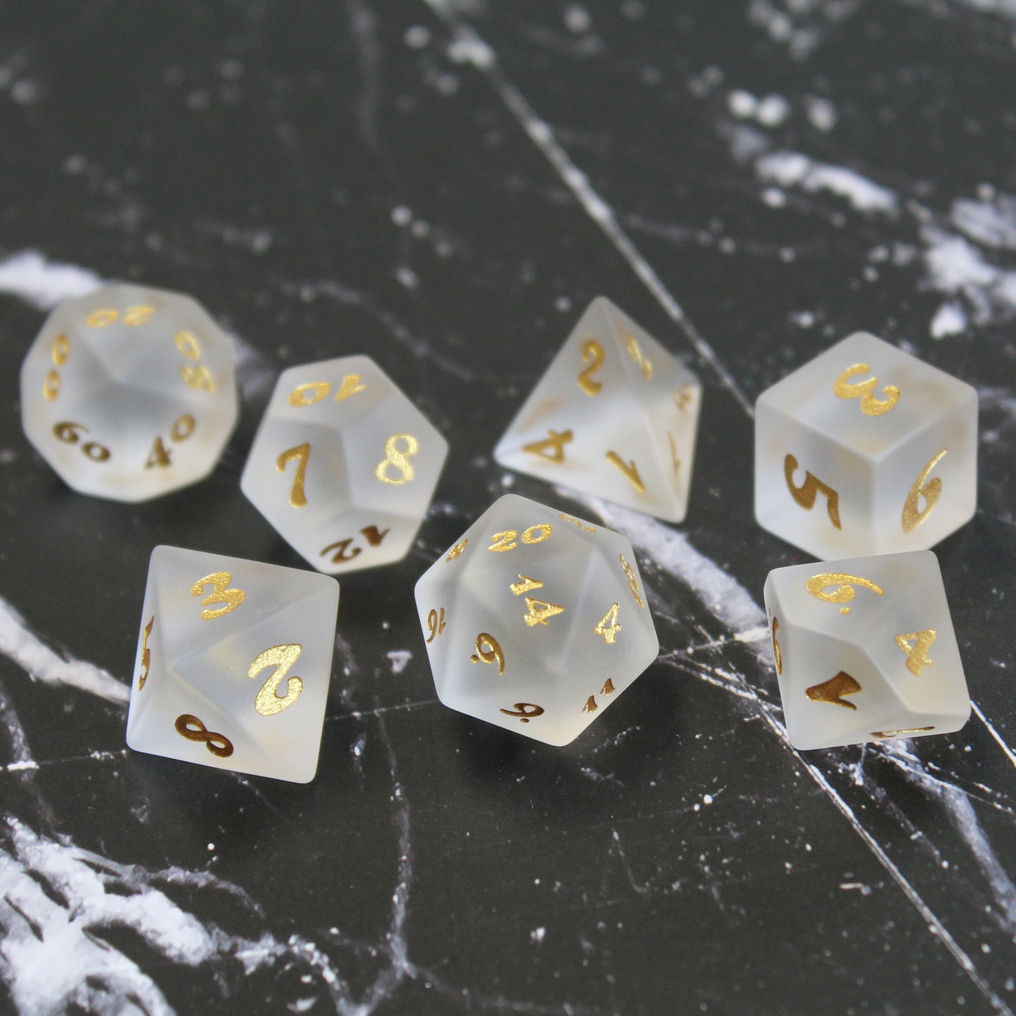 Set of white frosted glass RPG dice with golden font on a black and white marbled background