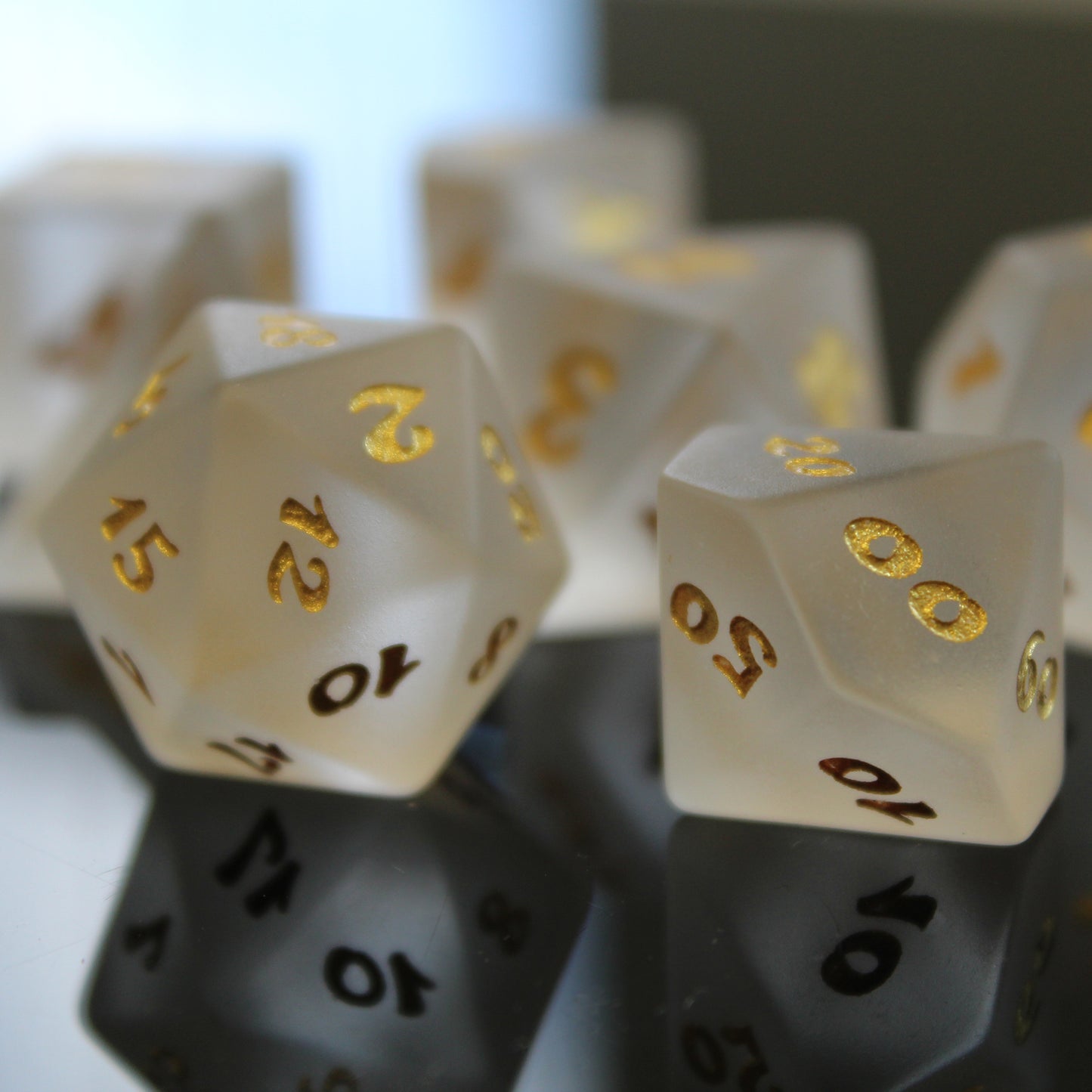 Closeup of a set of white frosted glass RPG dice with golden font on a mirror