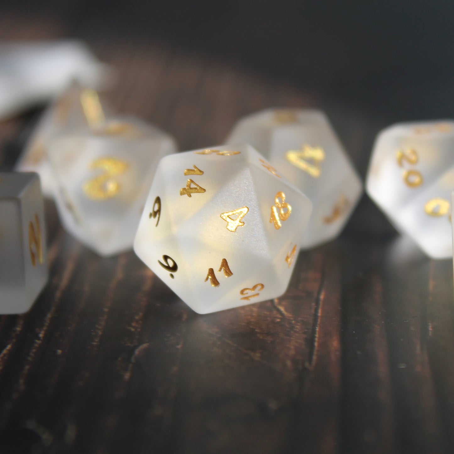 A closeup of a Set of white frosted glass RPG dice with golden font on a wooden background