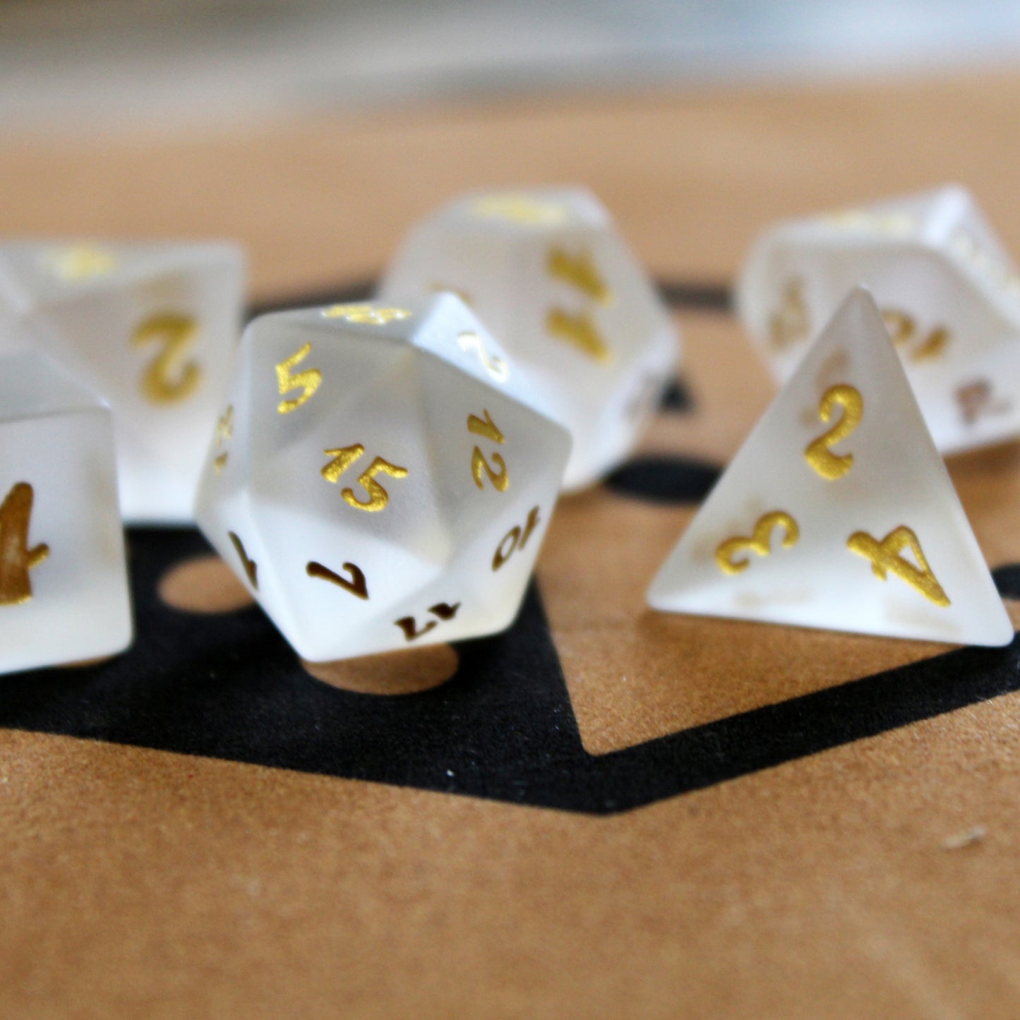 Closeup of a set of white frosted glass RPG dice with golden font on a brown felted tray with the Dice Dungeons logo
