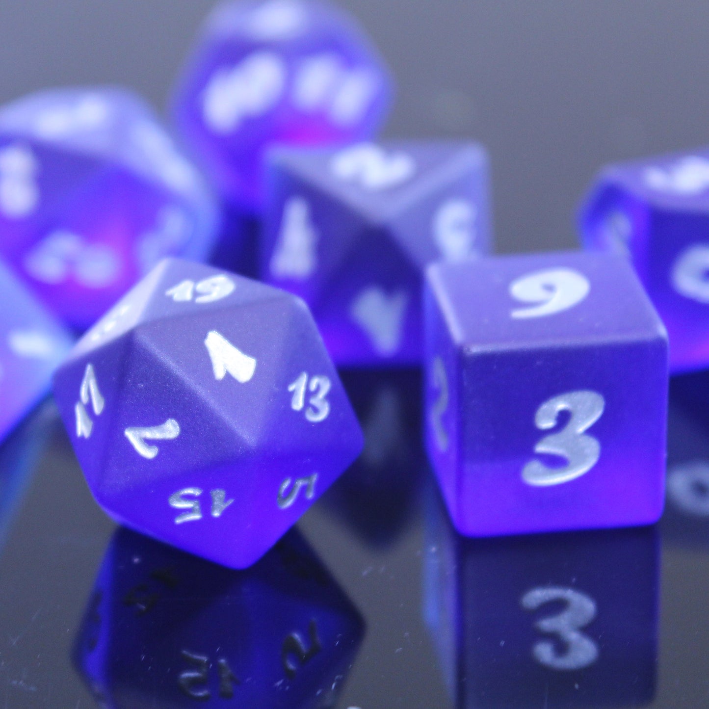 Closeup of a set of dark blue translucent glass RPG dice with silver numbering on a mirrored surface