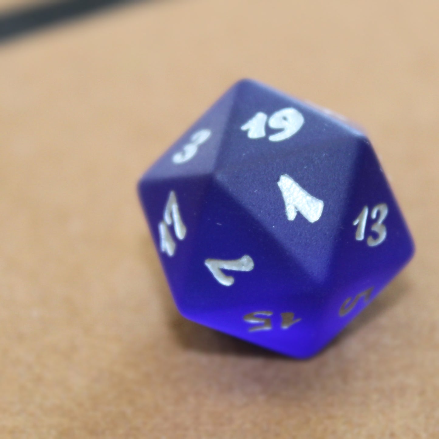 A closeup of a dark blue translucent glass twenty-sided die with silver numbering