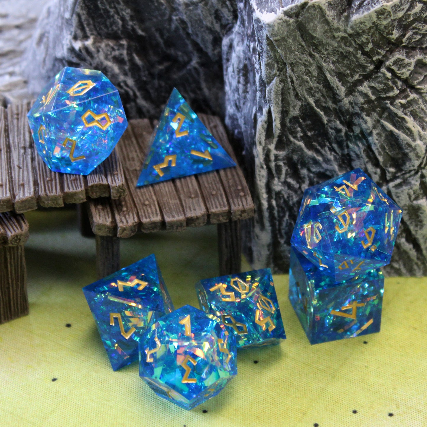 Blue StarGlow dice set arranged on a wooden step set piece. Some of the pieces are on top of the steps while others are in front on the green game mat. In the background is some rocky wall set pieces.