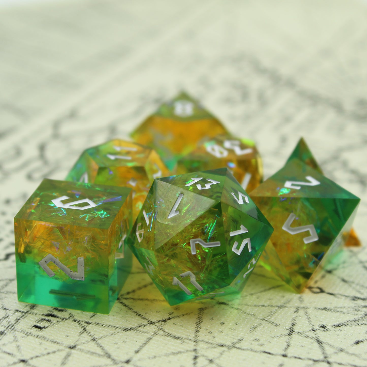StarGlow Mutation Green Sharp Edge Resin Dice Set displayed on an antique map, highlighting the iridescent inclusions and silver Roman-inspired numbering against the blue-green resin.