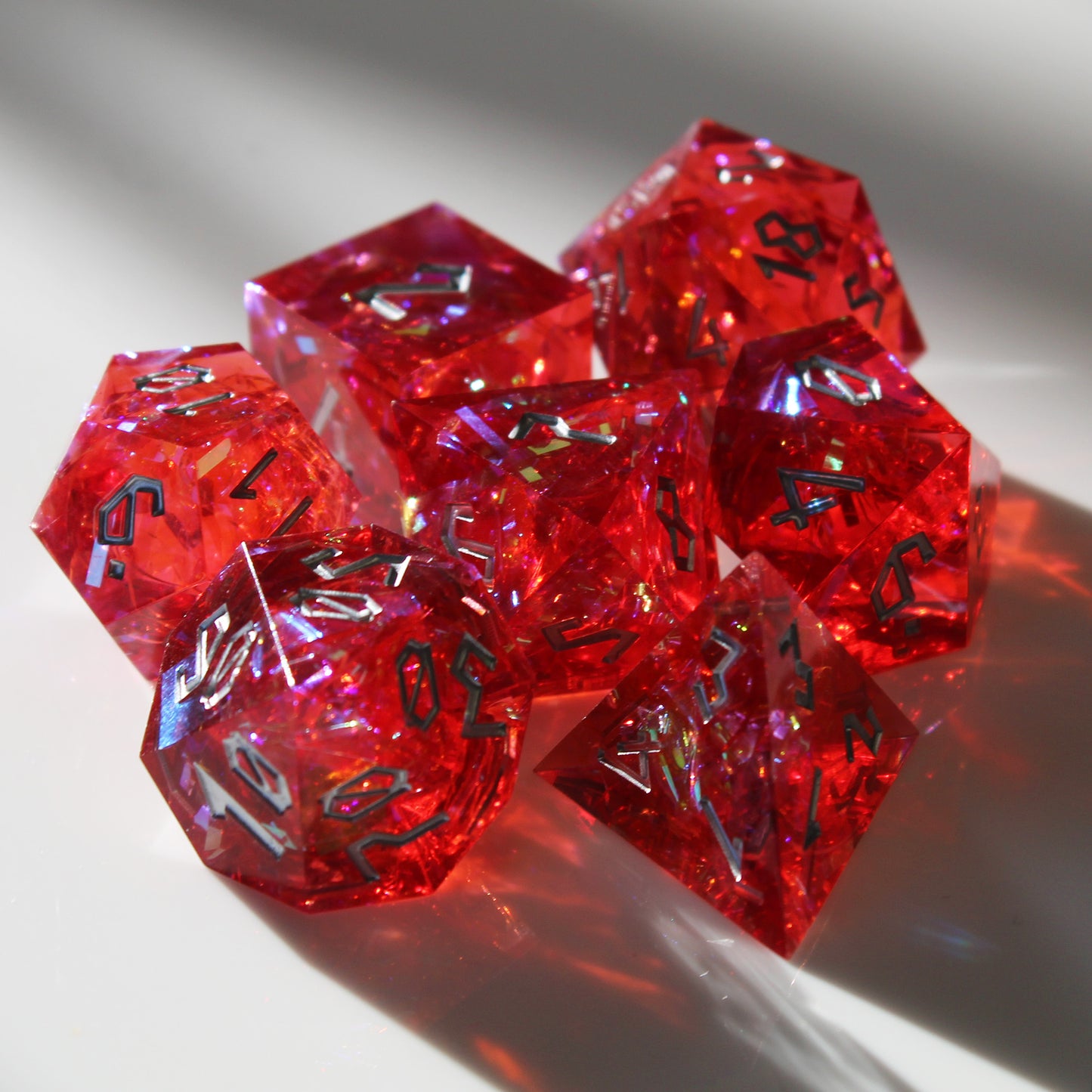 Grouped StarGlow Red resin dice set with light shining through, highlighting the red resin and iridescent inclusions.