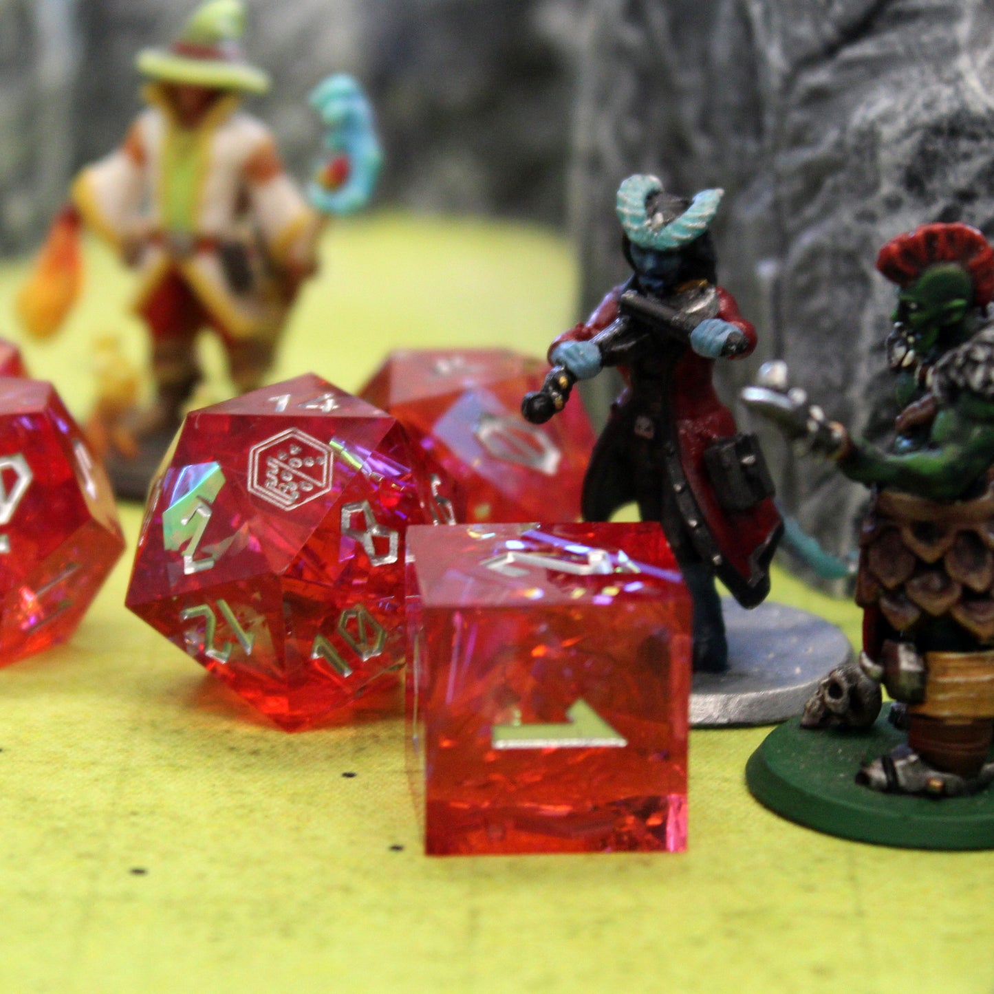 StarGlow Red D6 on a table with miniatures nearby, highlighting the translucent red resin and silver inking.