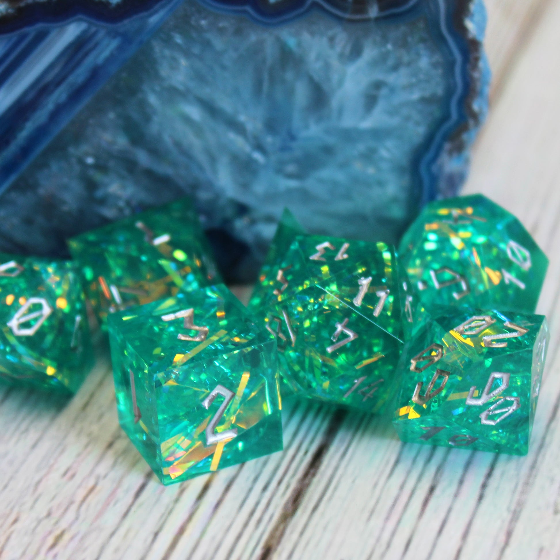 StarGlow Turquoise dice set on a wooden table, with blue-green resin and silver numbering.