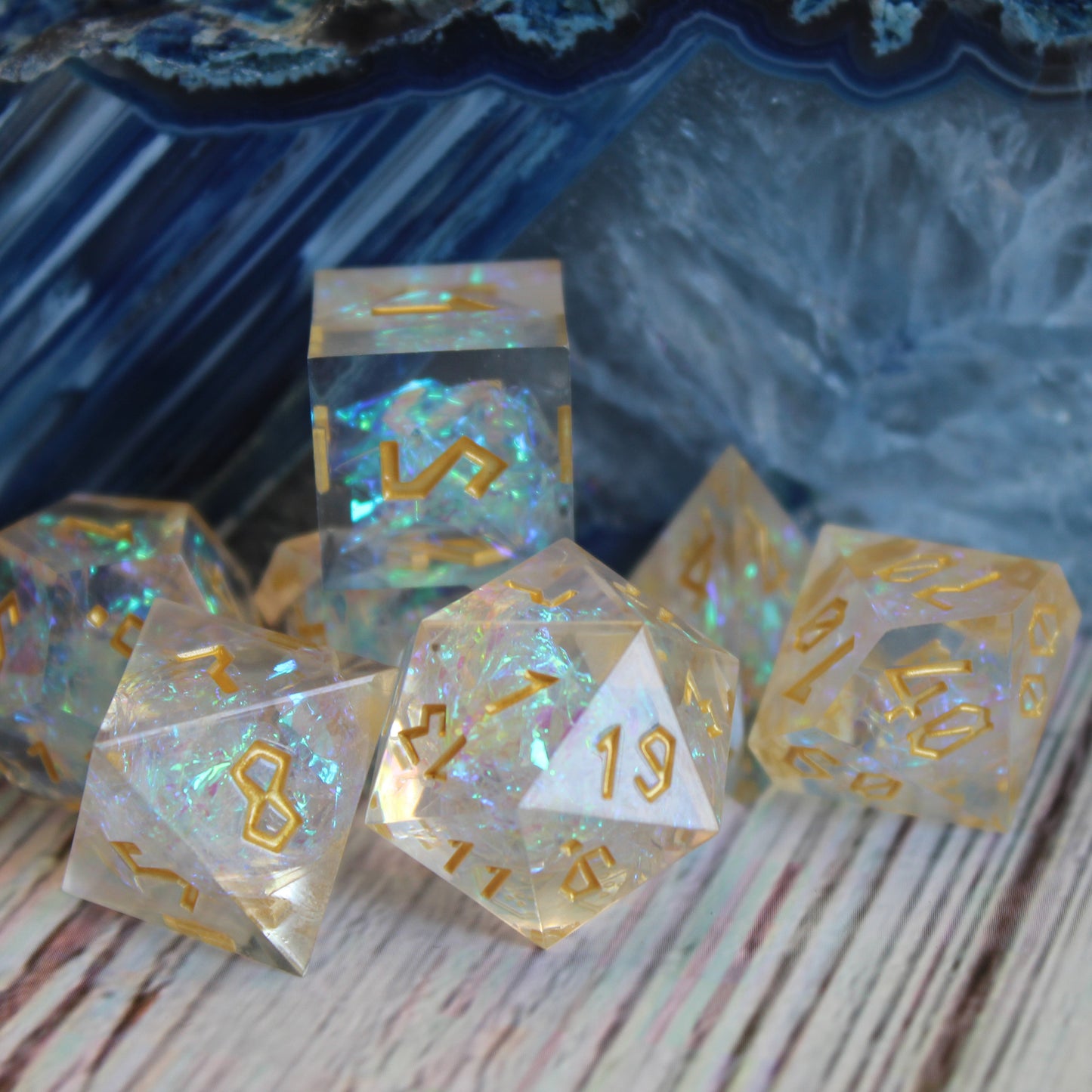 StarGlow White dice set arranged on a white wood surface with a polished multi-colored blue and white stone behind it.