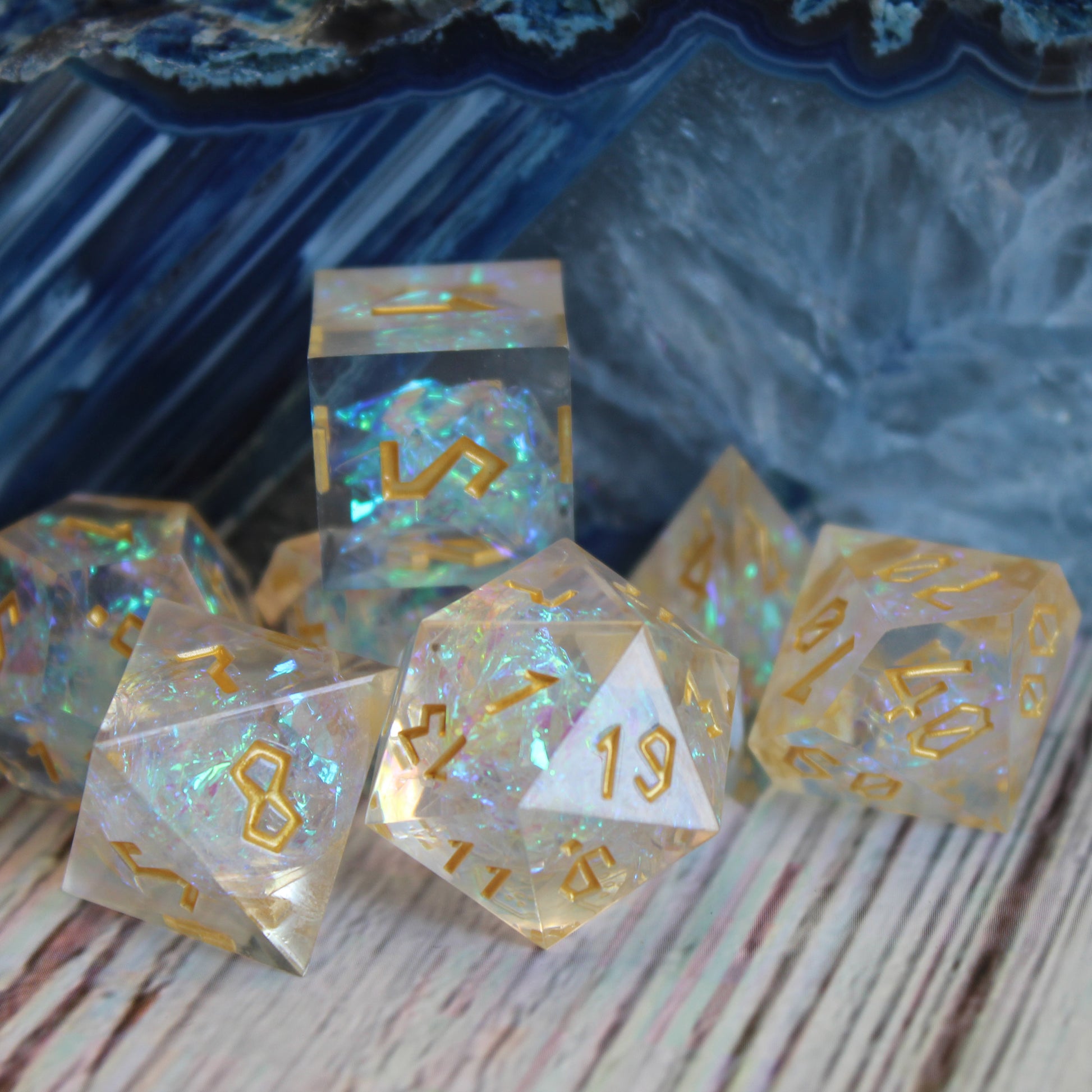 StarGlow White dice set arranged on a white wood surface with a polished multi-colored blue and white stone behind it.