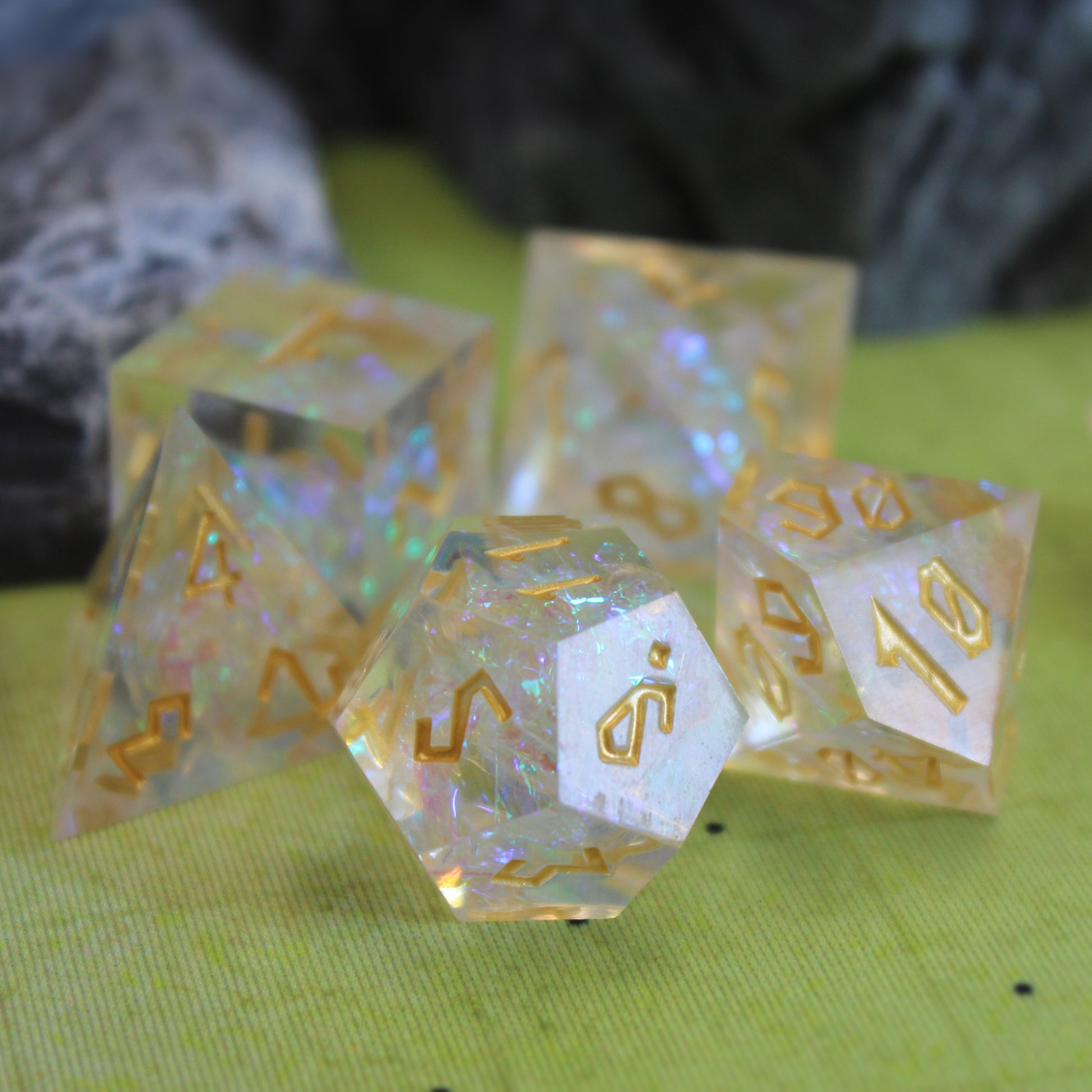 StarGlow White dice set arranged in a pile on a green game mat with gray rocky set pieces behind it.