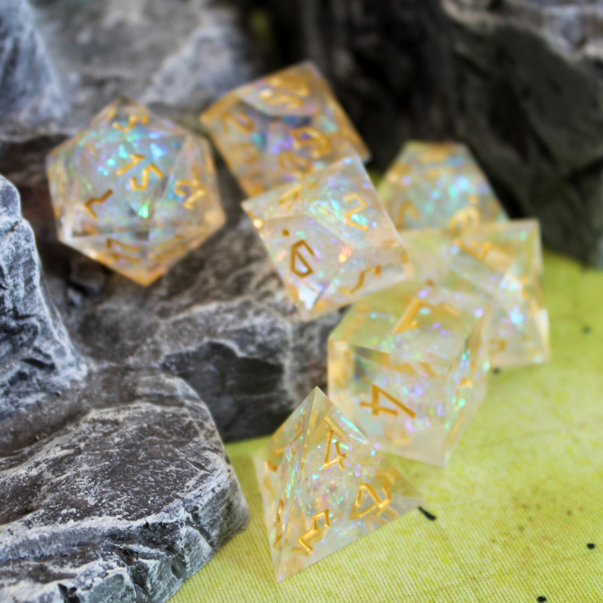 StarGlow White dice set arranged on top of and in front of a gray rocky set piece, to look as if the dice are tumbling down it. All items are on top of a green game mat.