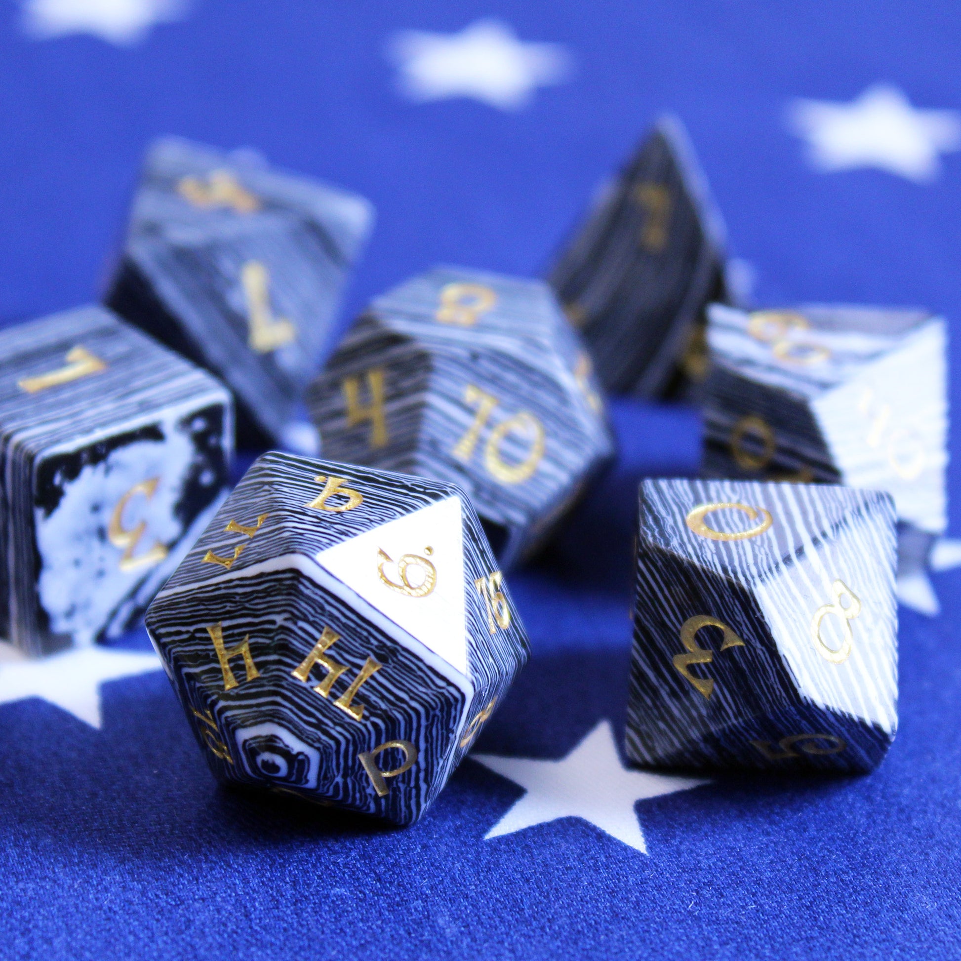 Black and White Striped Dice with Gold Numbering on a Blue Fabric Background