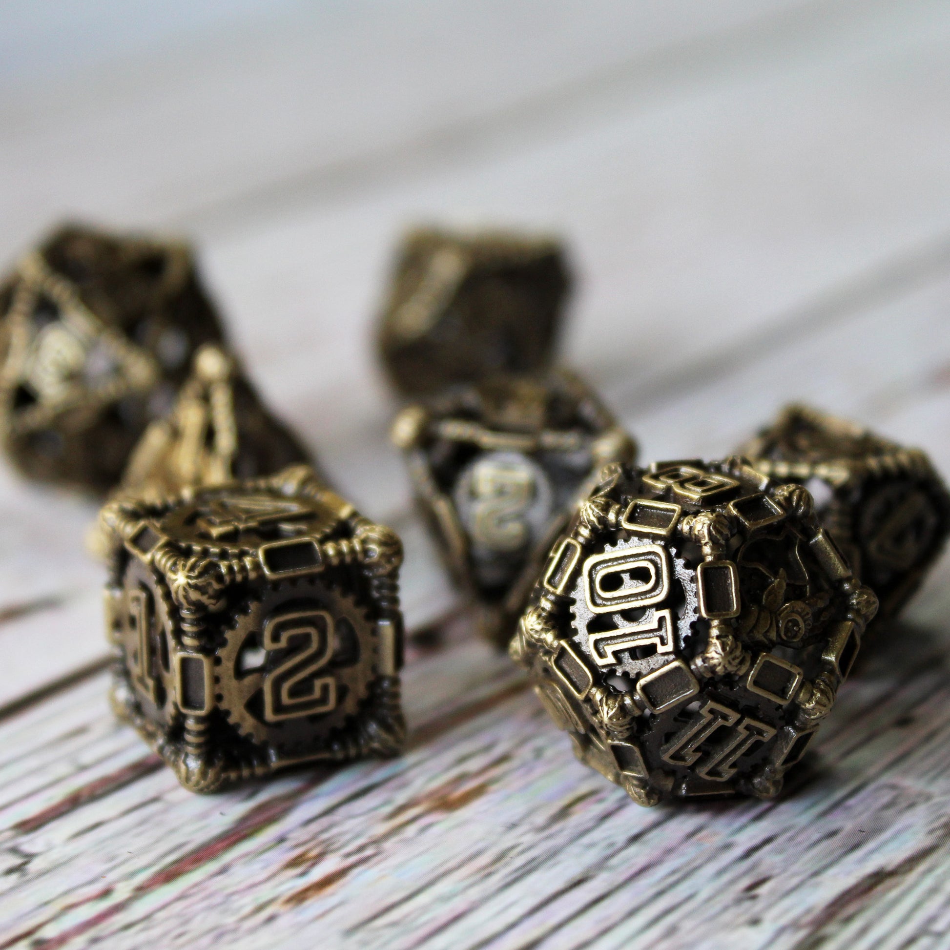 6 sided die and 12 sided die in foreground, with other 5 die blurred in background. All on a white wood paneled surface.