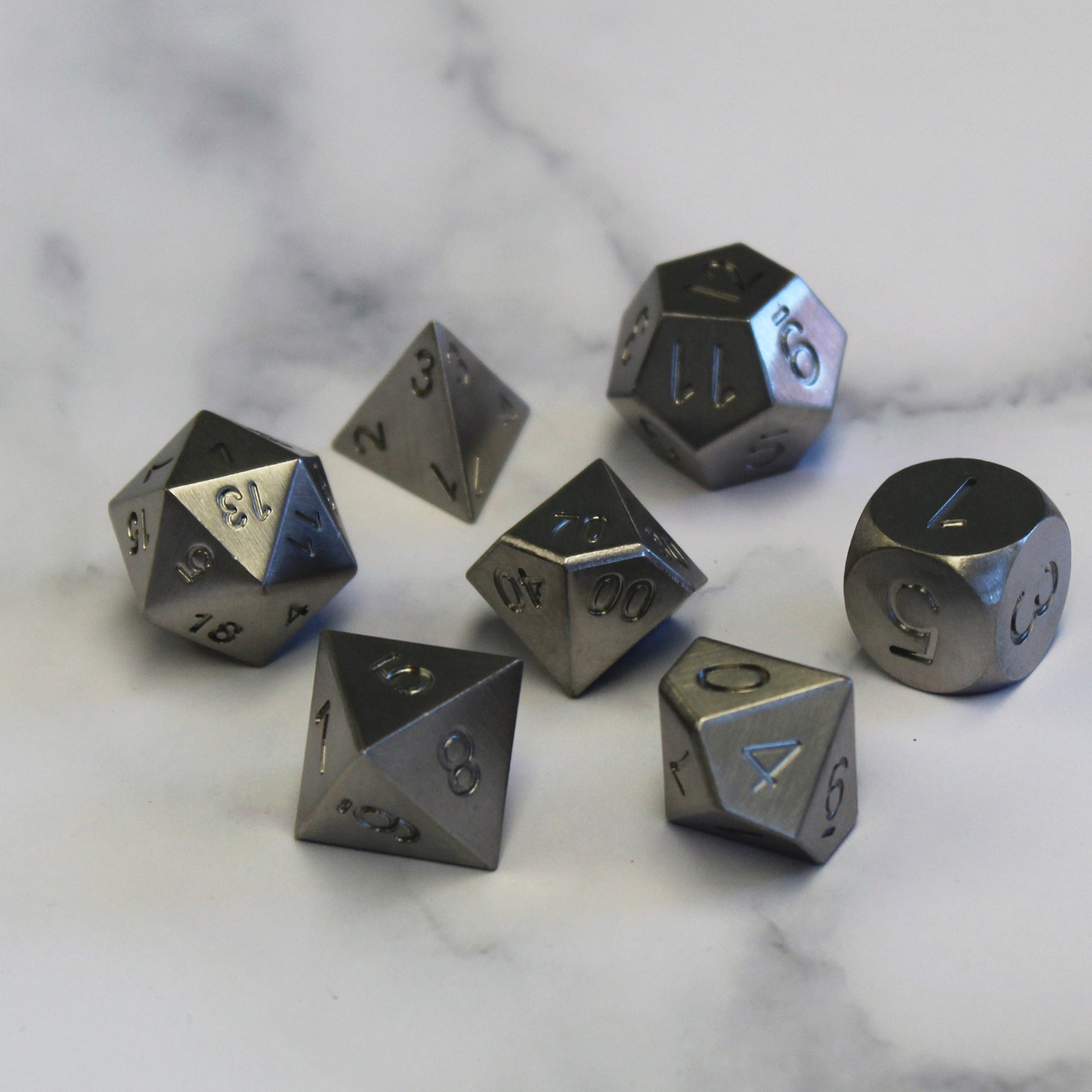 Solid Tungsten full RPG dice set resting on a white marble surface.