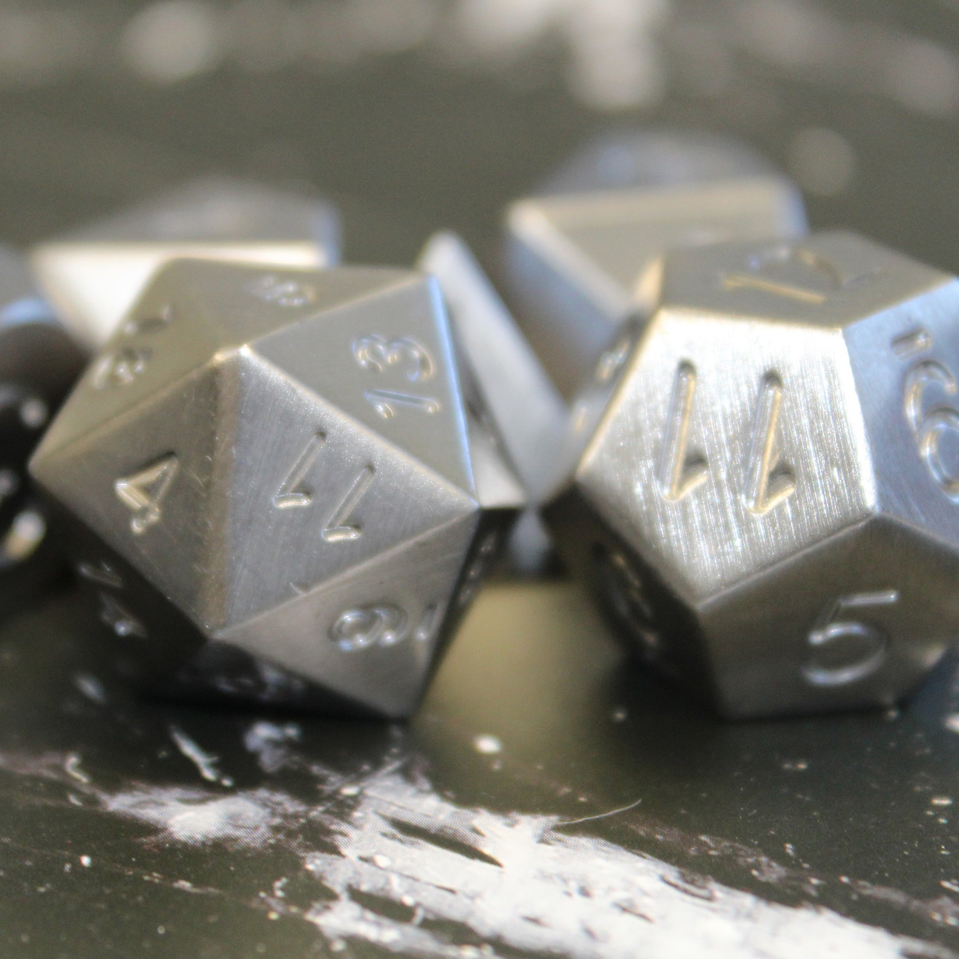 Close up detail shot of the d20 and d12 with lighting highlighting the brushed metal surface of the Tungsten dice set. Both faces of the dice show the 11 face.
