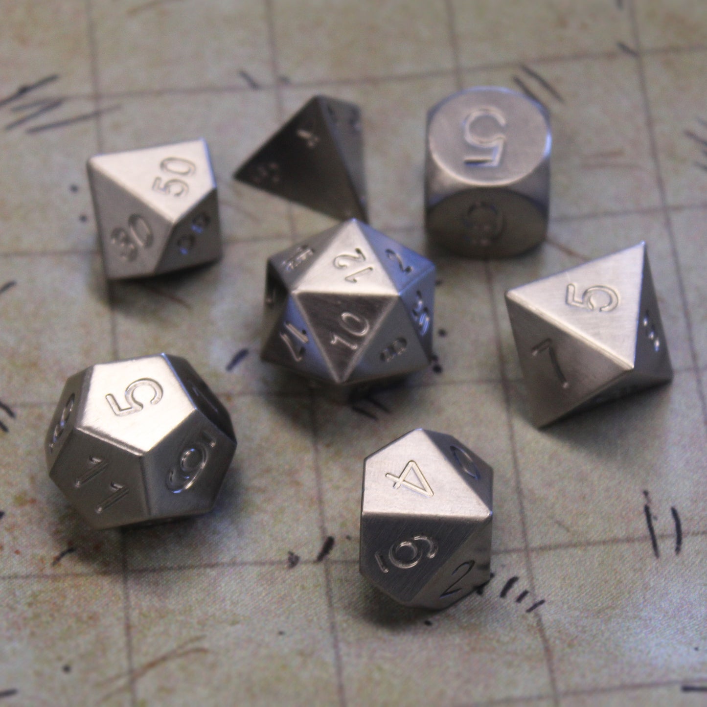 Tungsten Dice arranged in a hexagon shape with the d20 central resting on a 1 inch map grid viewed from above. Tungsten is also know as Wolfram.