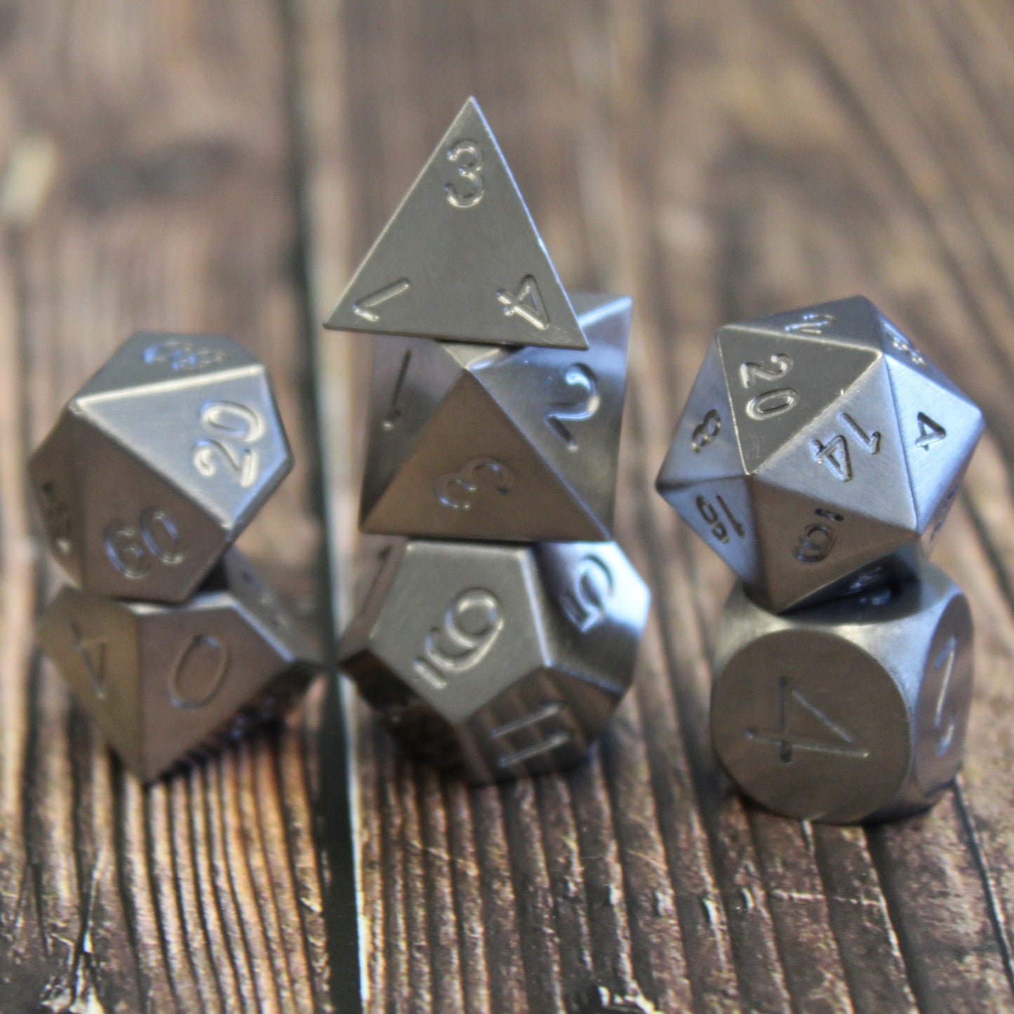 Full metal Tungsten RPG set arranged in stacked columns resting on a wooden surface. The d4 is highlighted at the top central position showing the non-2 face on 3.