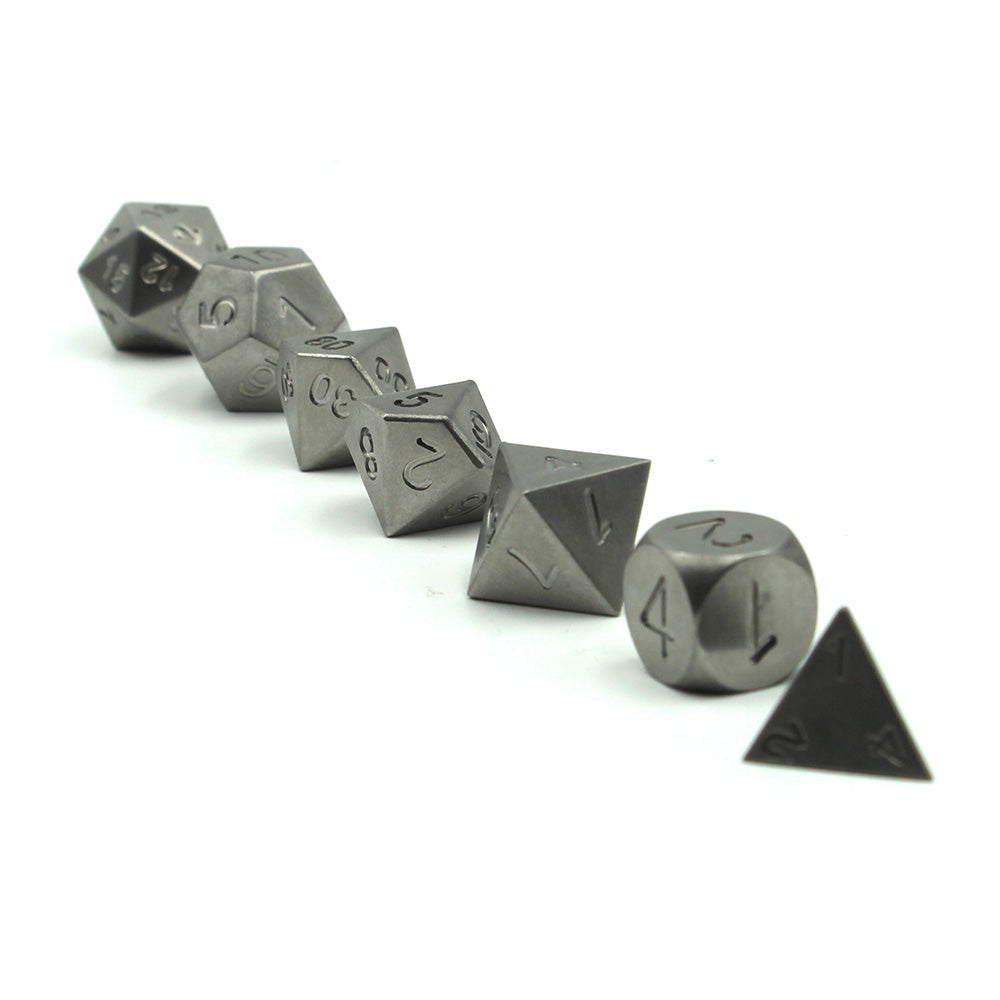 Metal Tungsten Dice Set arranged in a line from lowest in the front to highest in the rear resting on a white surface.  The heaviest dice in our lineup and one of the few without electroplating or inking to highlight the base metal of their construction.