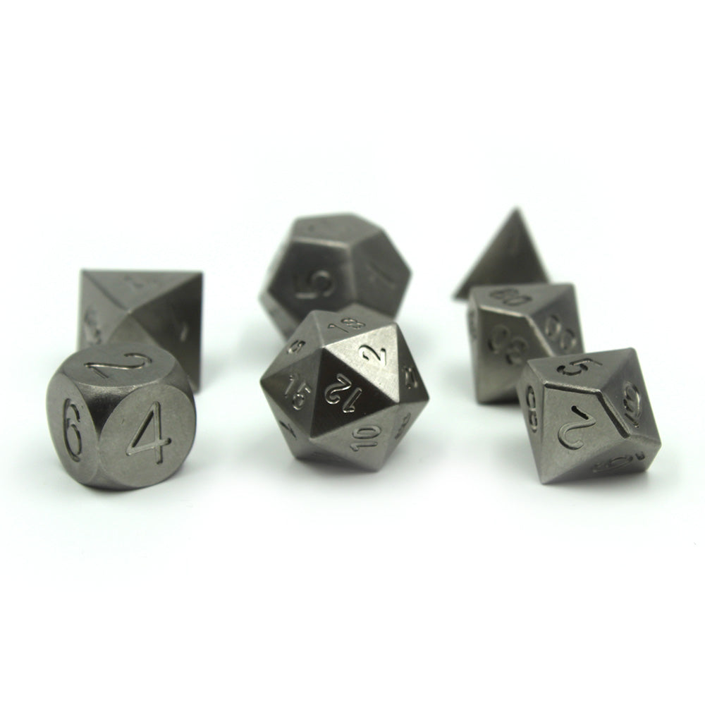 Metal Tungsten Dice Set on a white surface with overhead lighting. The d20 is center with the 12 face towards the viewer flanked by the d6 and d10 of the set.