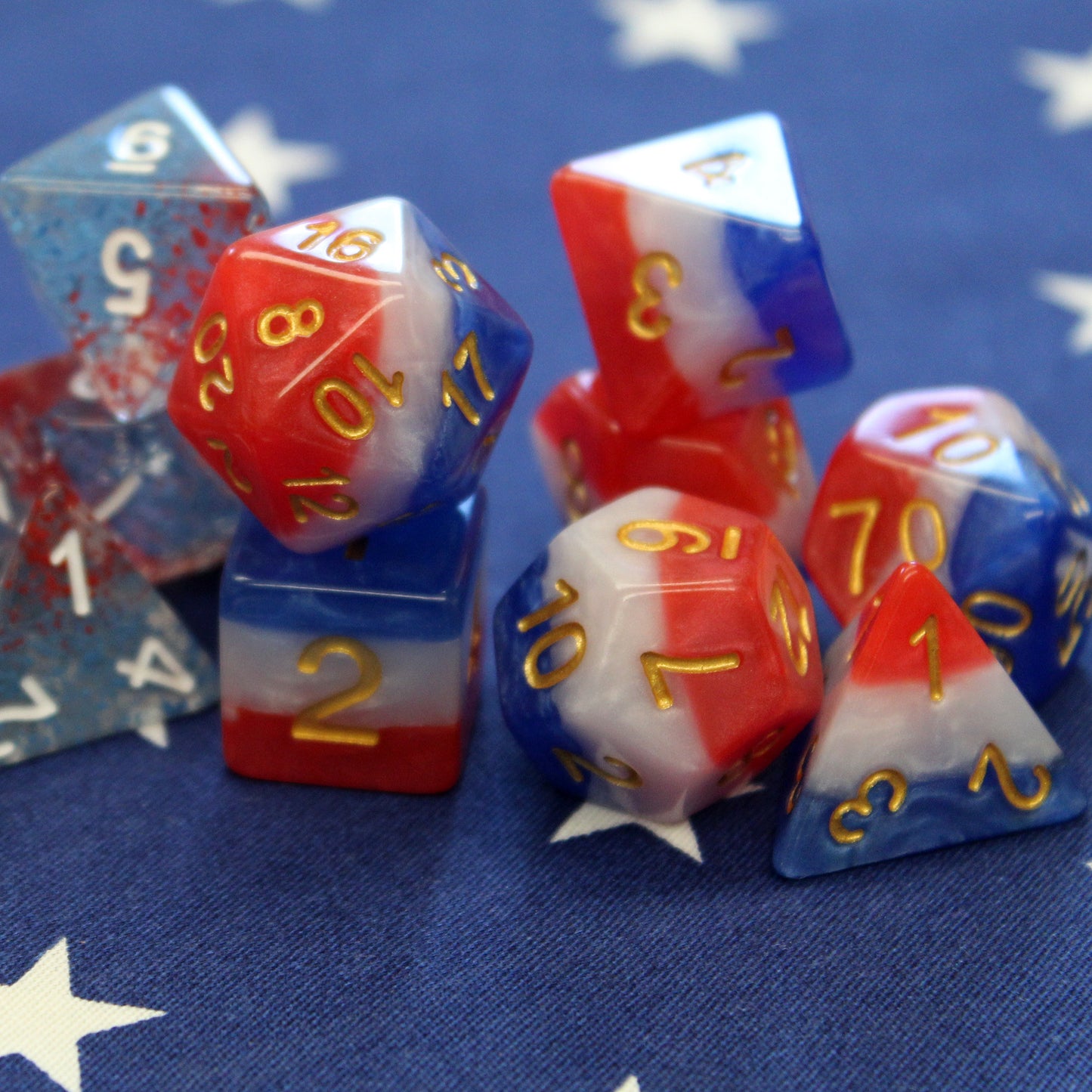 Layered red, white, and blue dice set resting on a blue flag with white stars, with a second set of dice in the background for comparison.
