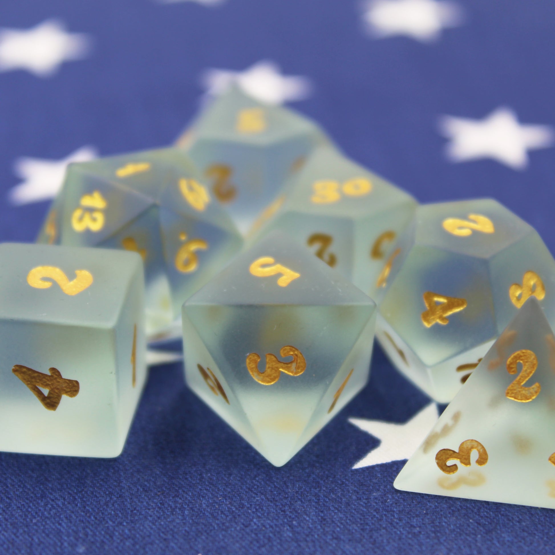 Close Up of a Set of Powder Blue Frosted Glass Dice with gold Numbering on a Blue Fabric Background
