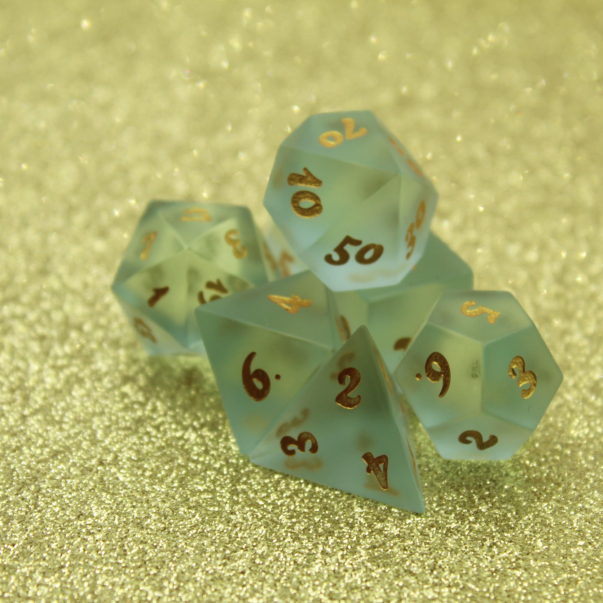 Set of Powder Blue Frosted Glass Dice with Gold Numbering .  Dice Set Pictured on a Gold Bakcground.