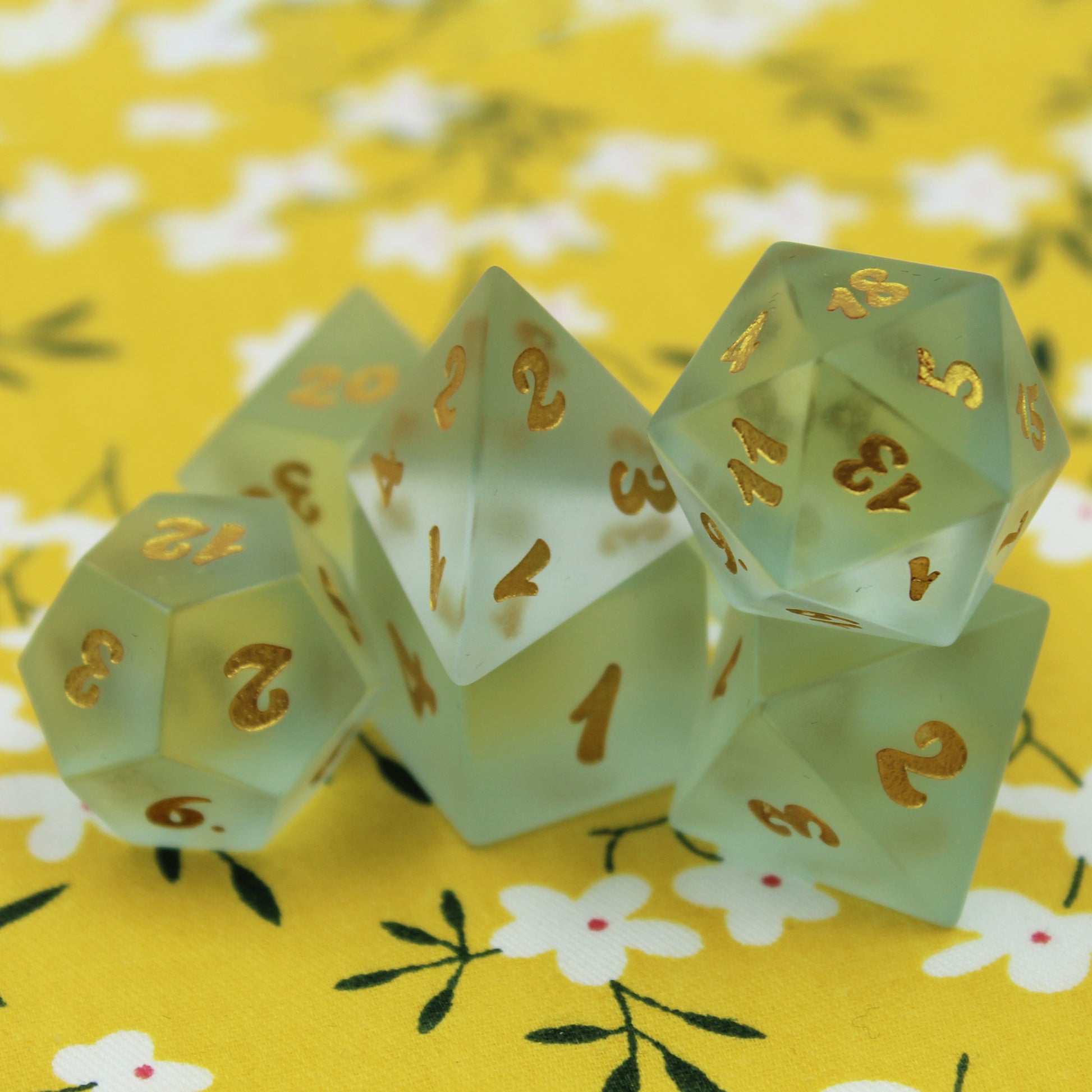 Set of Powder Blue Frosted Glass Dice with Gold Numbering on a Yellow Fabric Background