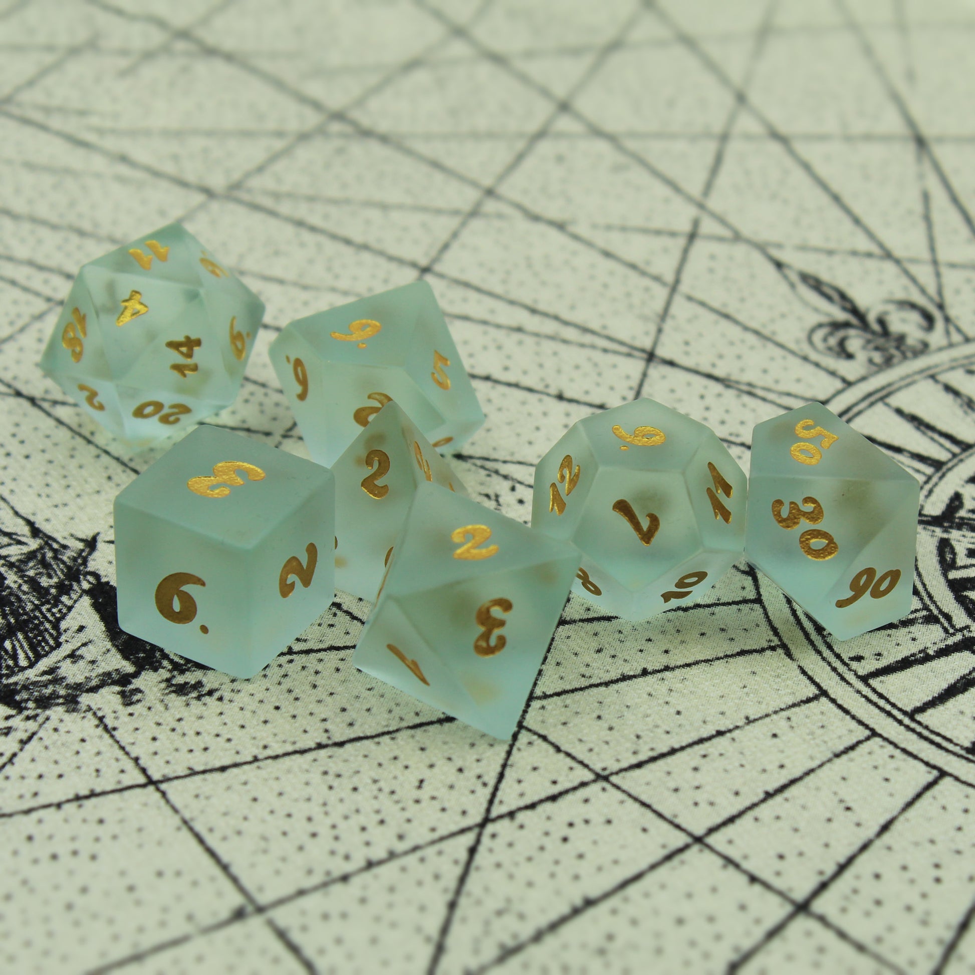 Set of Powder Blue Frosted Glass Dice with Gold Numbering on a Parchment Background