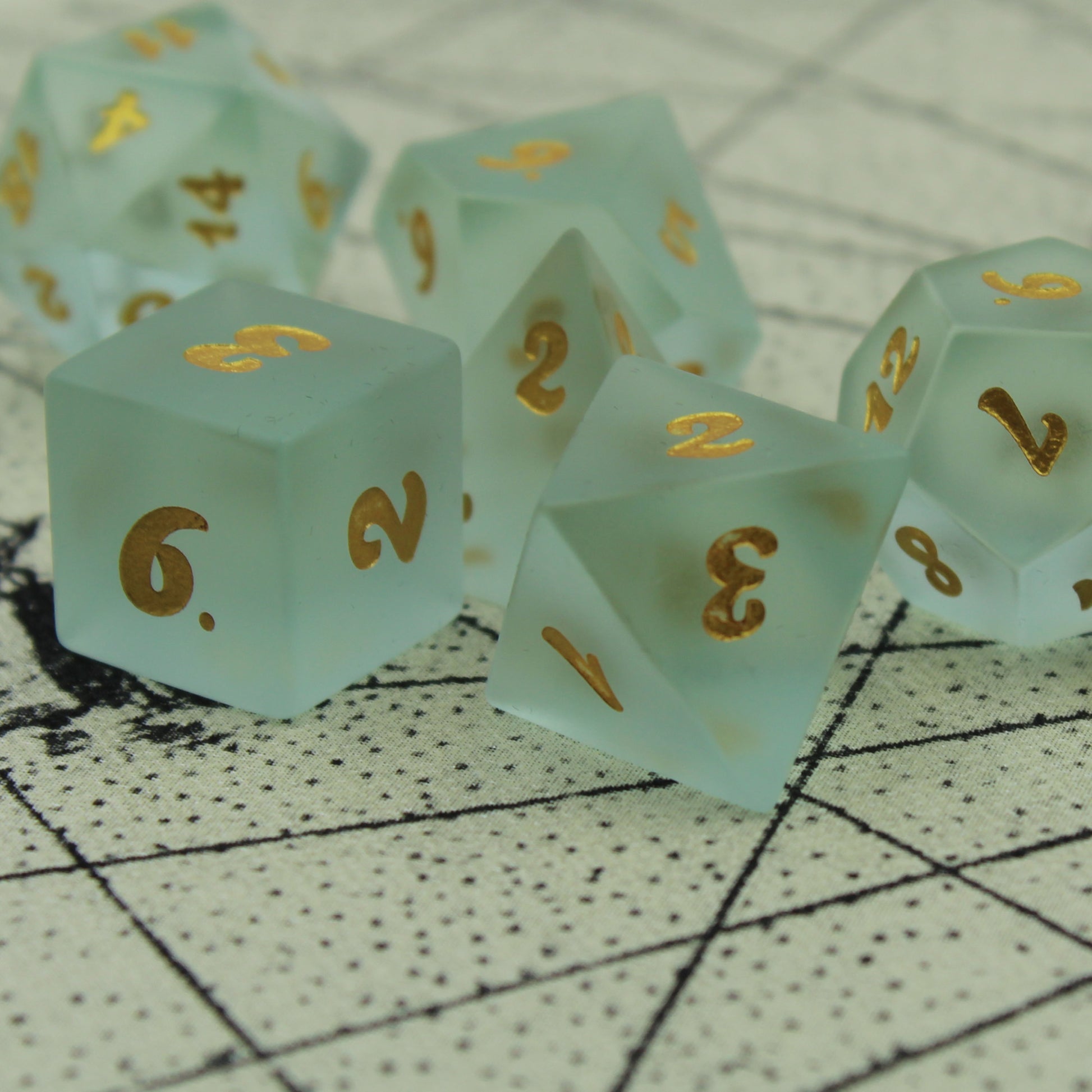 Close up of a set of powder blue frosted glass dice with gold numbering on parchment background.