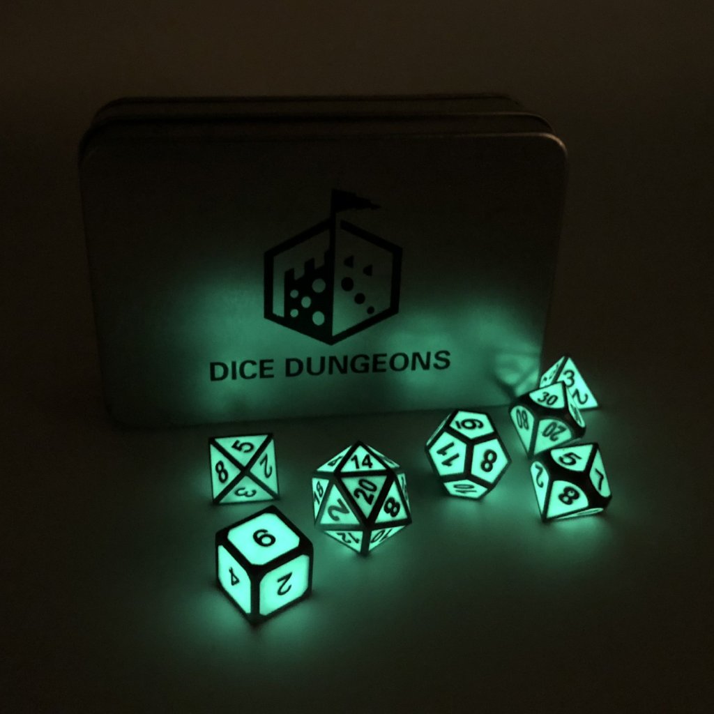 Metal Imperial Glow in the Dark dice set in the dark, with a Dice Dungeons silver display box propped up behind them. The glow from the dice is shining on the box, casting a green color.