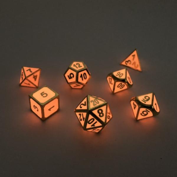 Imperial Glow in the Dark pink dice scattered on a white surface. In the dark, the dice are glowing a light pink color and the gold numbers and framing look dark.
