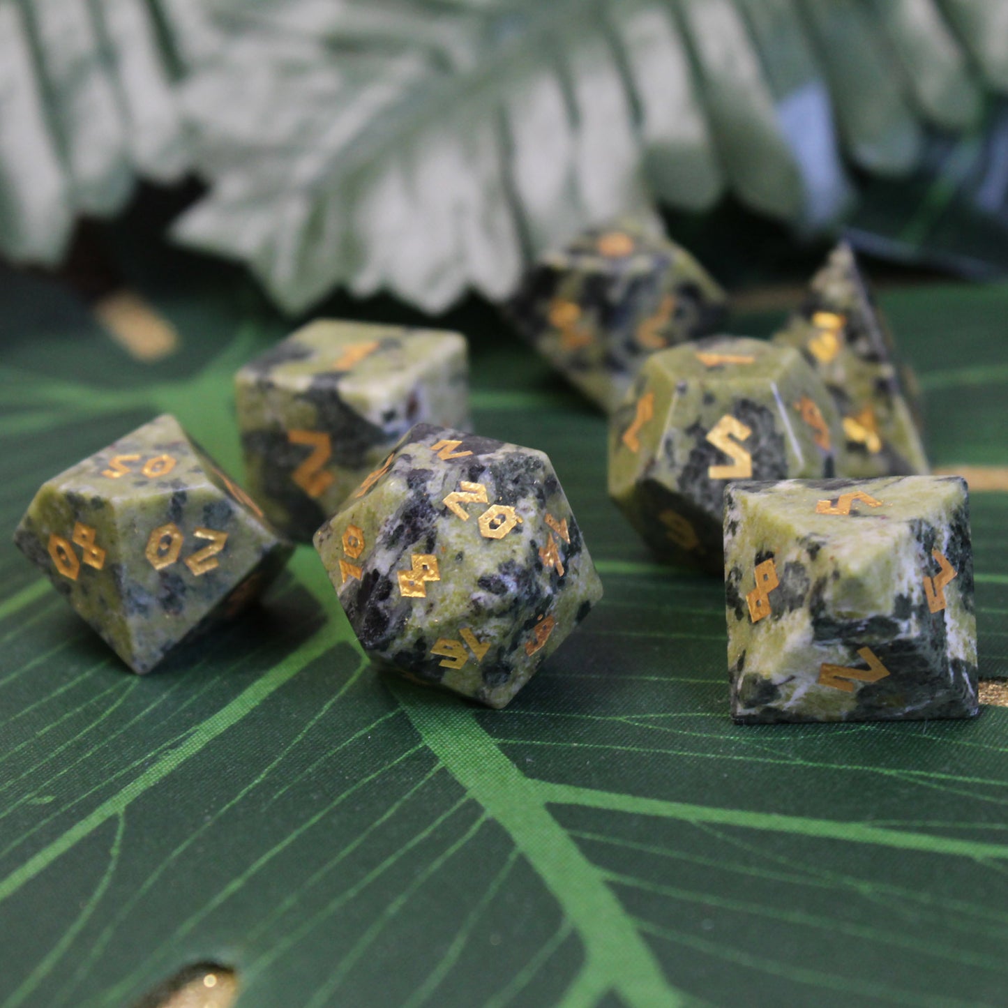 Brazilian Jade dice set on a green backdrop, showing the jade’s natural color and gold numbering.