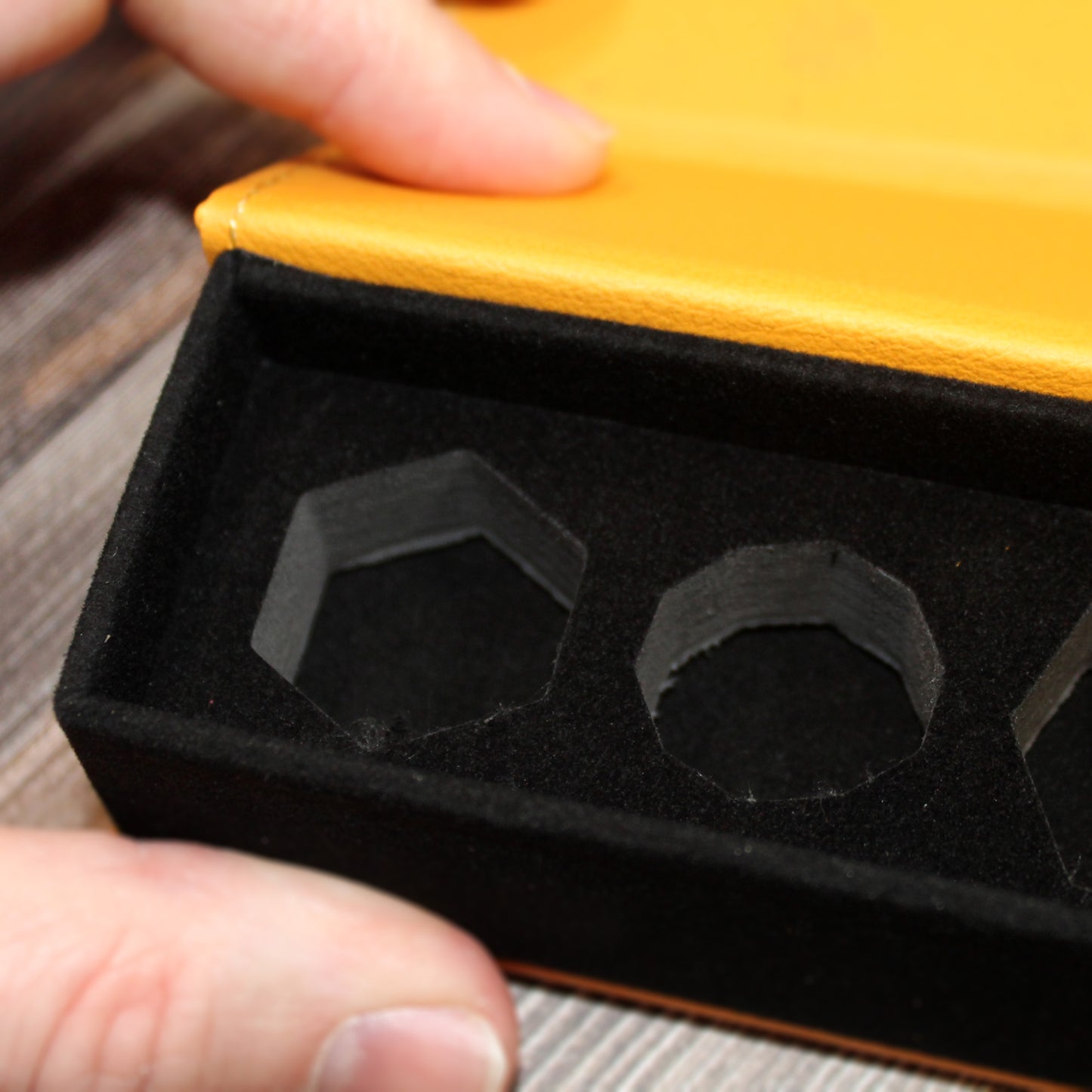 Black interior of dice case in a yellow PU Leather box held by a hand on a wooden surface