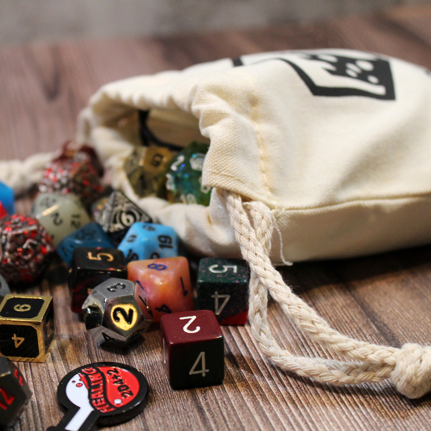 A full cotton dice bag laying down with a variety of polyhedral dice spilling from its opening.