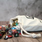 The side view of a full cotton dice bag laying down with a variety of polyhedral dice spilling from its opening.