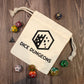 An off-white cotton drawstring bag with a hexagonal castle logo and the words "Dice Dungeons" printed on it. Several polyhedral dice are spread around the bag, and it is laying flat on a wooden surface.