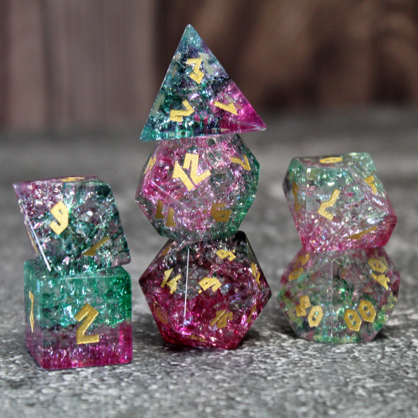 Stacked Frost Bound Fae Friend Shattered Glass dice set, featuring flamingo pink and emerald green hues with intricate fissures that sparkle like Faerie Fire in the light.