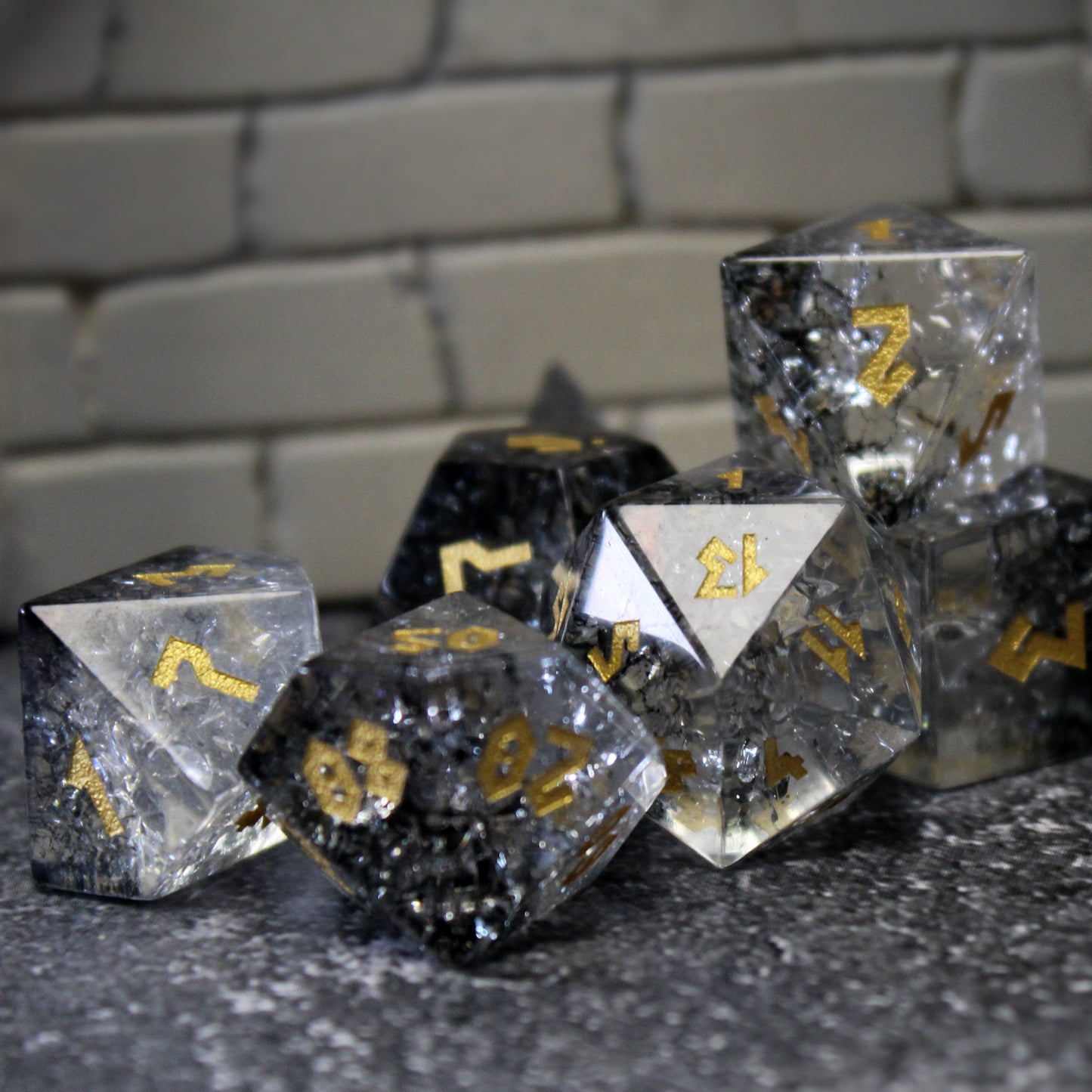 Full dice set in front of a stone wall, showcasing gold numbers contrasting with black and silver.