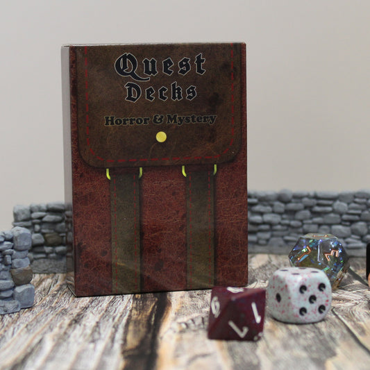 Photo of Quest Deck: Horror & Mystery physical deck box standing upright on a wooden surface with dice and walls on a white background.